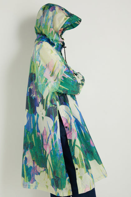 A person stands sideways against a plain white background, wearing the Lily Poncho—a hooded, waterproof rain poncho featuring a colorful abstract floral pattern.
