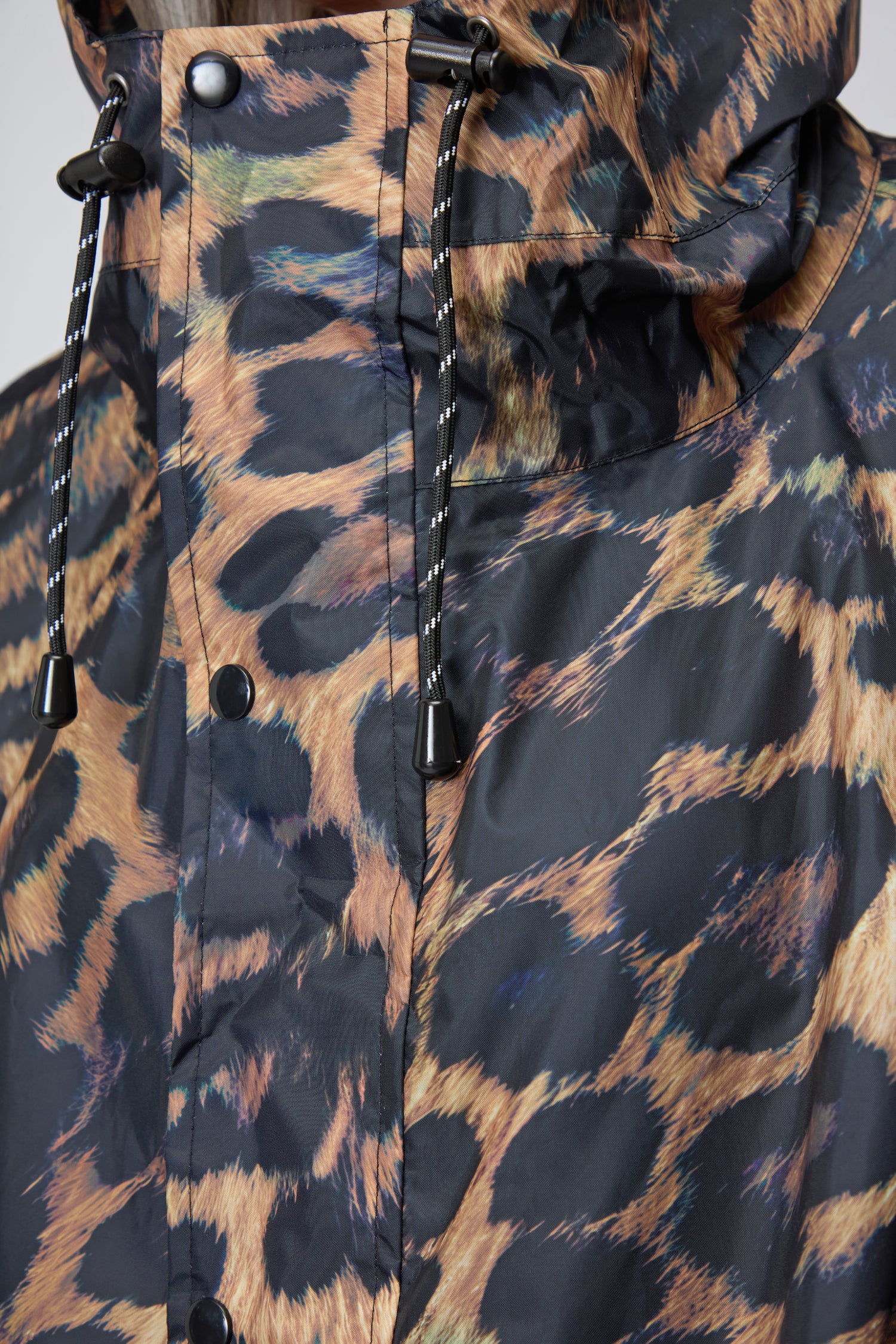 Close-up of the Dark Leopard Rain Coat, crafted from recycled polyester with a bold leopard print, black snap buttons, and hood drawstrings finished with black plastic tips.