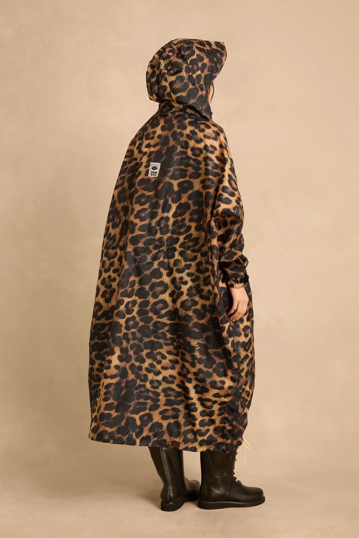 A person seen from behind wears an oversized, leopard-print Dark Leopard Rain Coat and black boots.