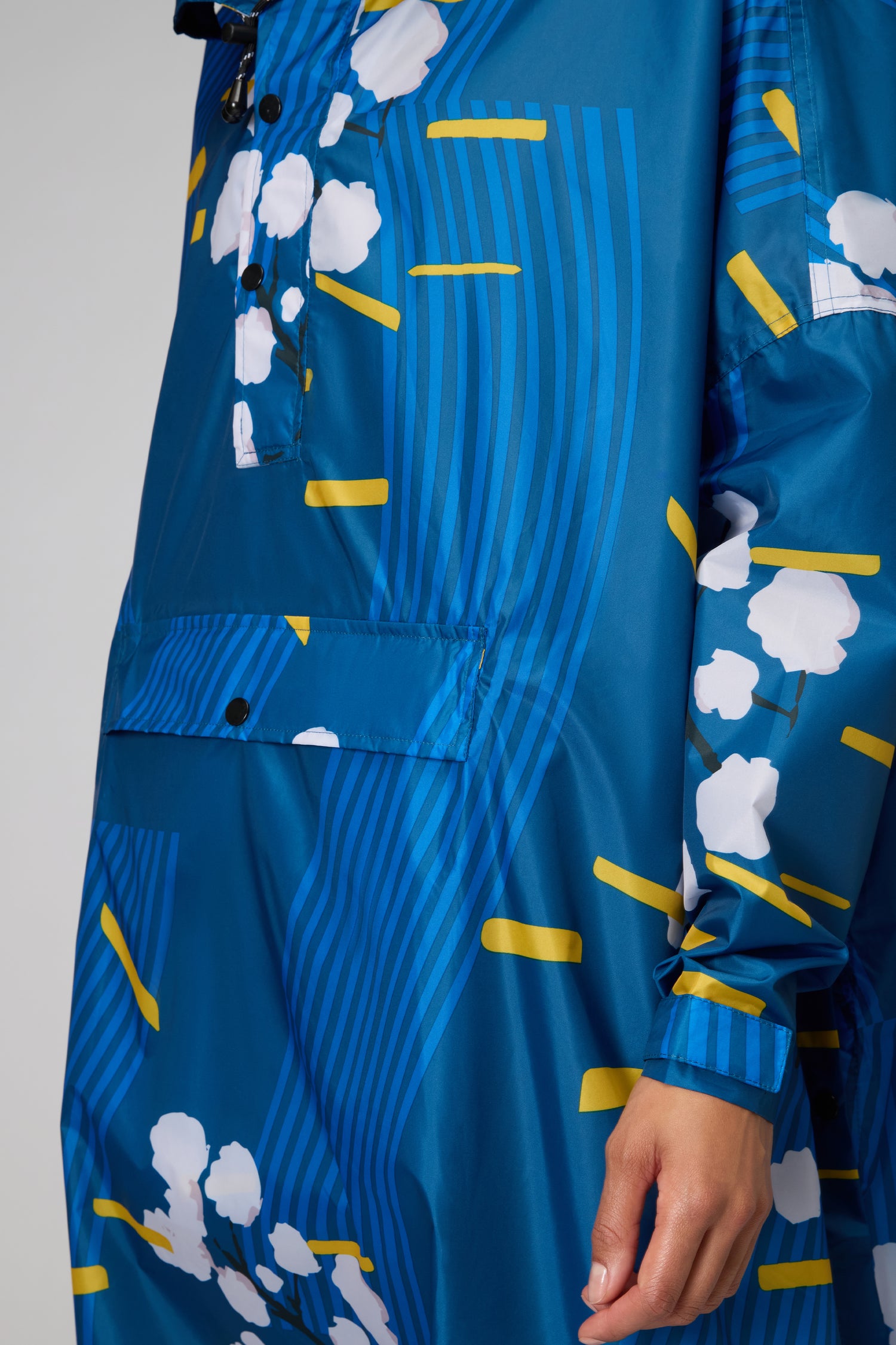 A person models the Japanese Blue Blossom Poncho, which features vertical blue stripes with white and yellow abstract patterns, visible from shoulder to mid-thigh.