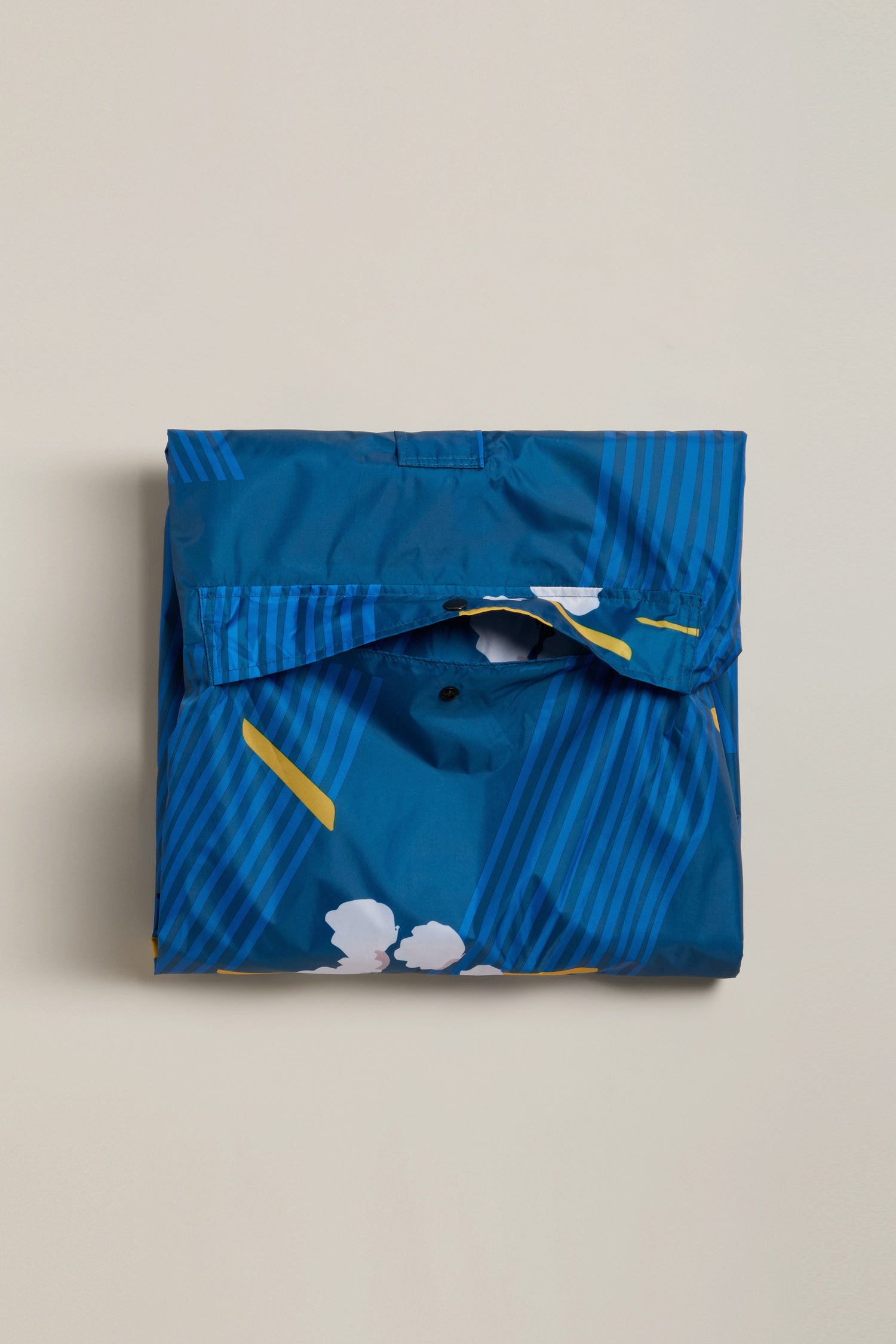 The Japanese Blue Blossom Poncho, made from recycled plastic, showcases blue fabric with yellow and white accents, displayed folded on a plain light background.
