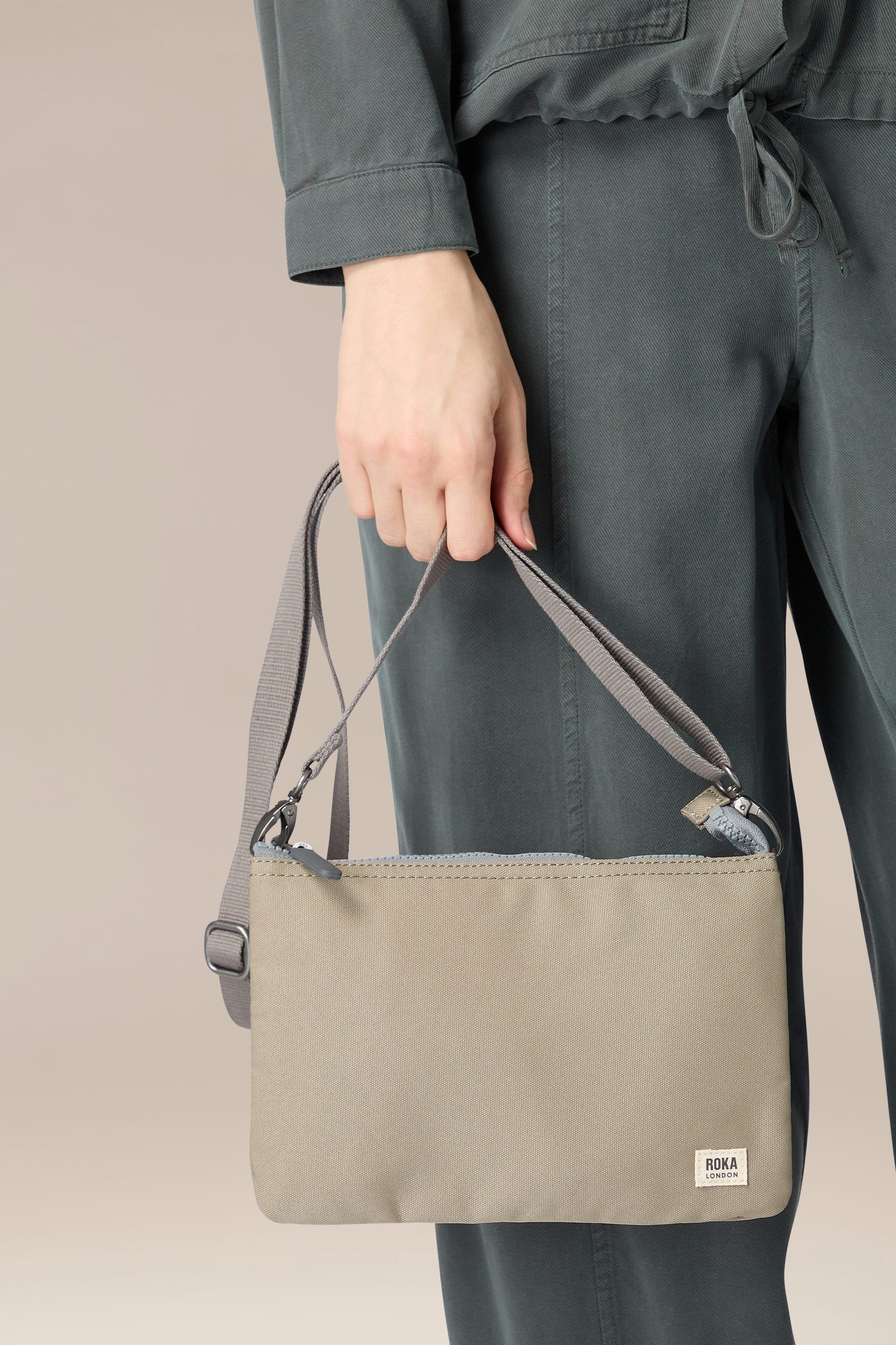 A woman is carrying a Recycled Carnaby Crossbody Bag in grey.