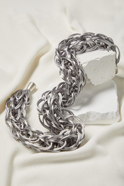 A Silver Woven Necklace, featuring a lightweight design, placed on top of a white piece of cloth.