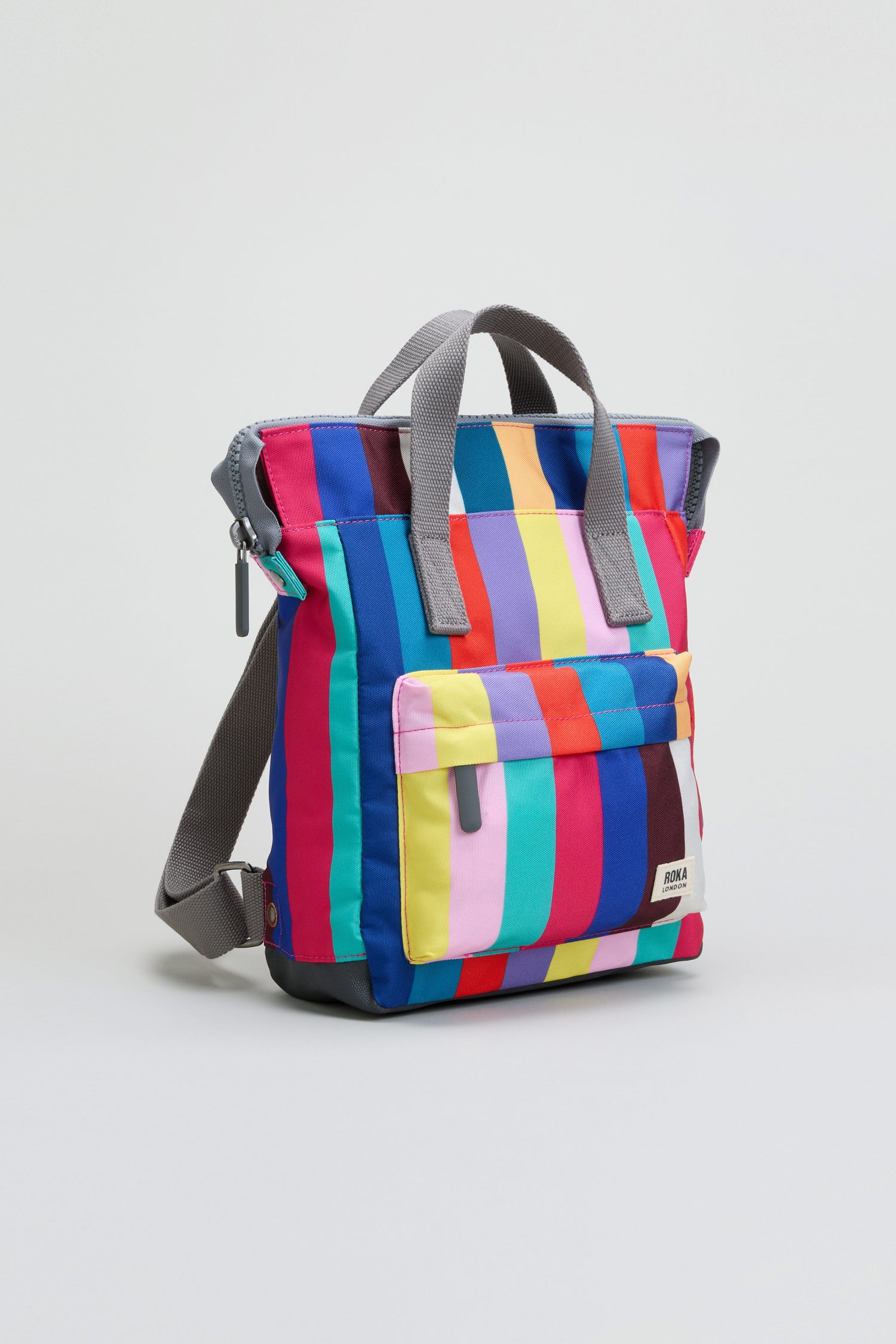 The Wide Multistripe Bantry Canvas Bag, featuring vertical rainbow stripes, gray handles, a front pocket, and a convenient laptop sleeve, is displayed on a plain white background.