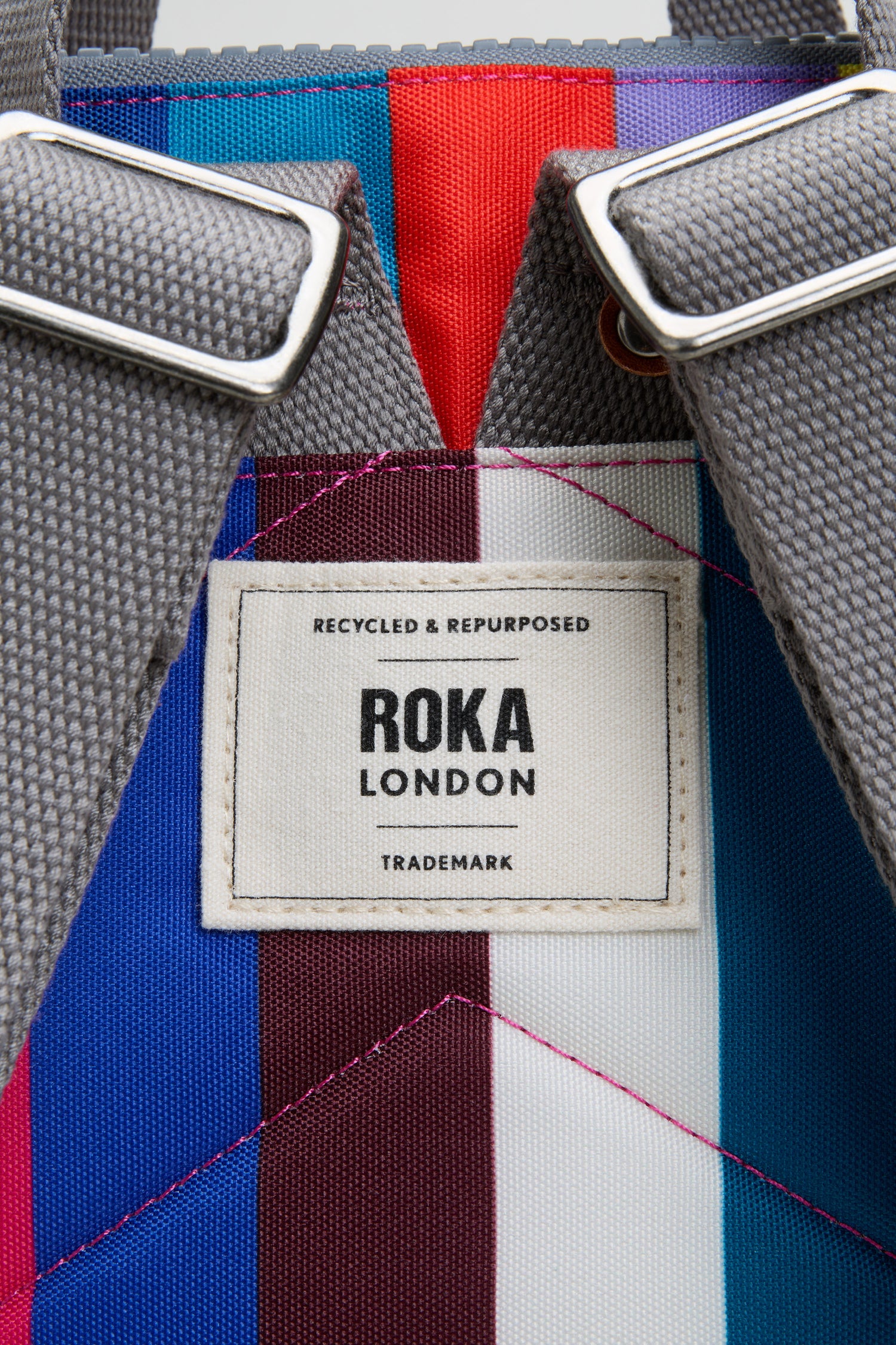 Close-up of the Wide Multistripe Bantry Canvas Bag, featuring colorful stripes, durable grey straps, and a white label reading “Recycled & Repurposed ROKA London Trademark.”.
