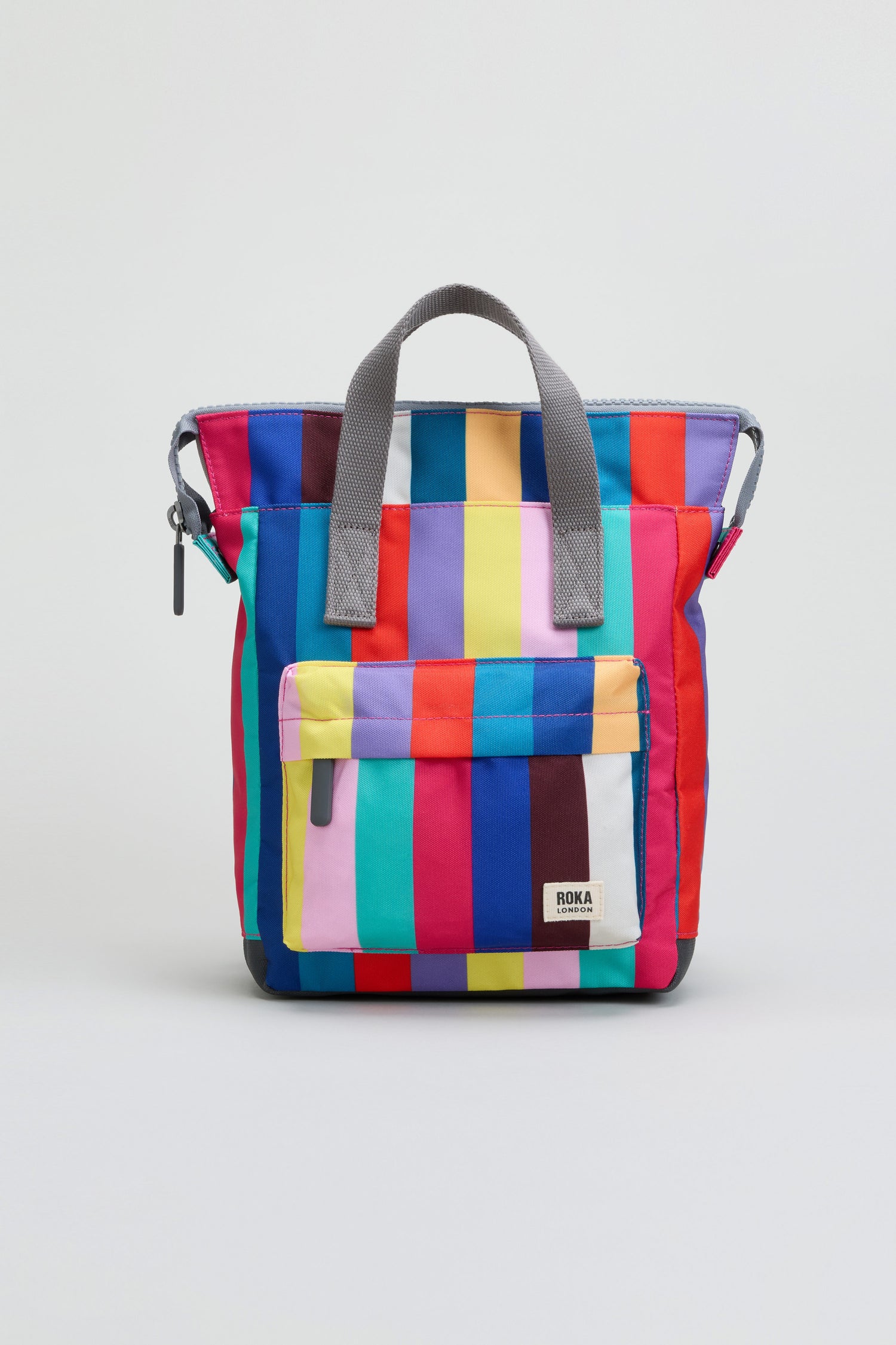 The Wide Multistripe Bantry Canvas Bag is a weather-resistant backpack featuring vibrant vertical rainbow stripes, gray handles, a front zipper pocket, and a white label with the “ROKA” brand. It also includes a convenient laptop sleeve for added functionality.