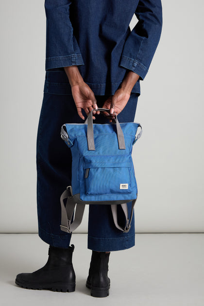 A person in a denim outfit holds the Recycled Canvas Stripe Bantry Bag by its handle, highlighting its eco-friendly design.