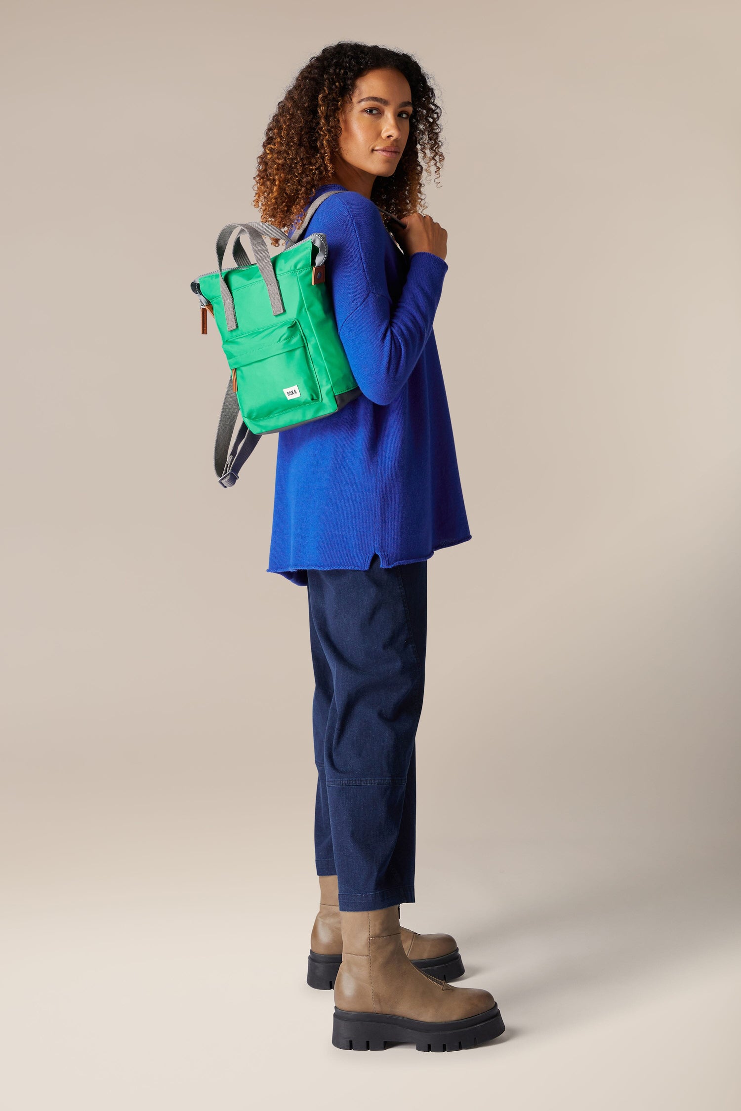 A woman in a blue shirt and boots is holding a green Recycled Bantry Bag.