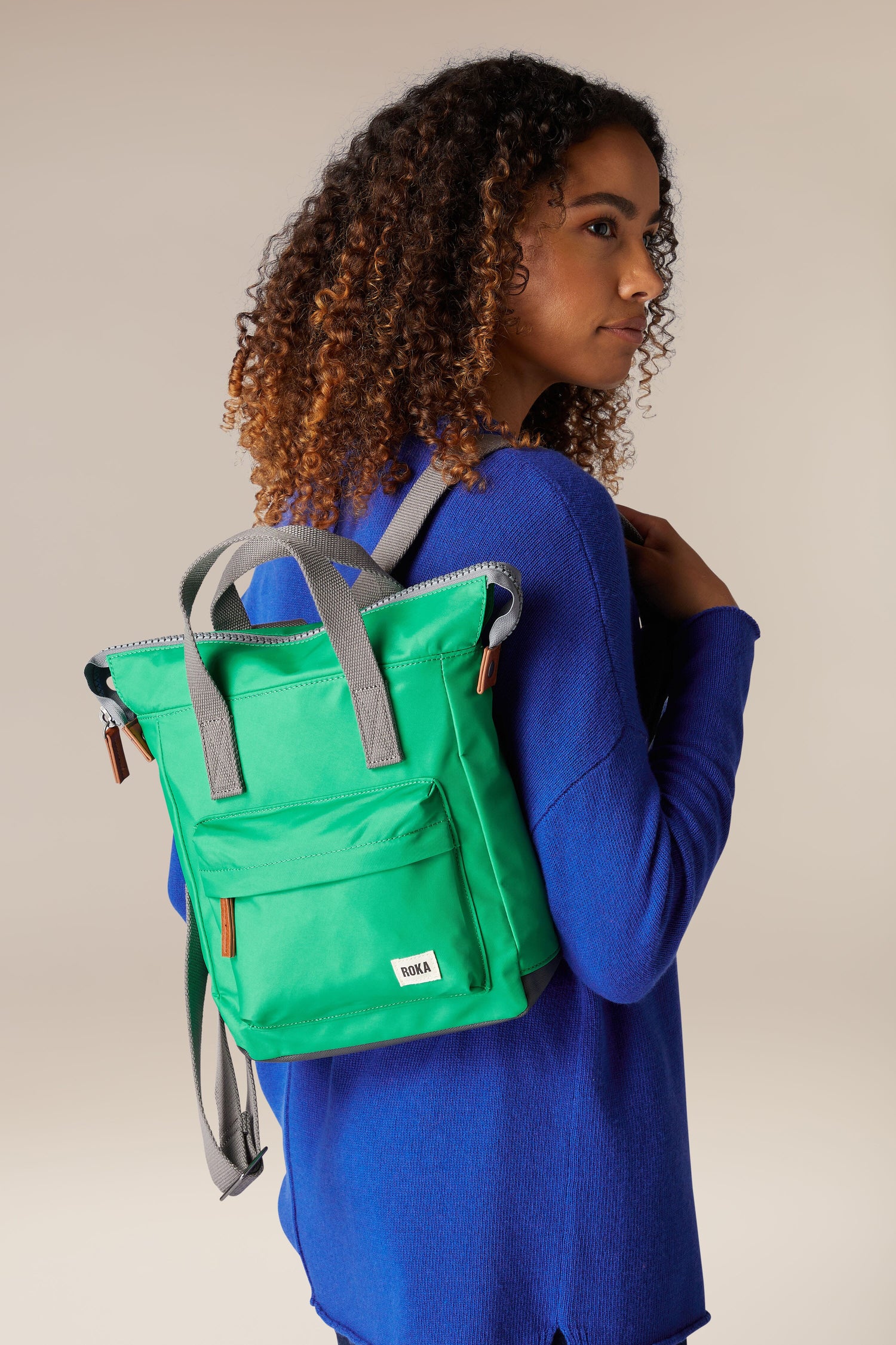 A young woman wearing a weather-resistant green Recycled Bantry Bag made of recycled nylon.