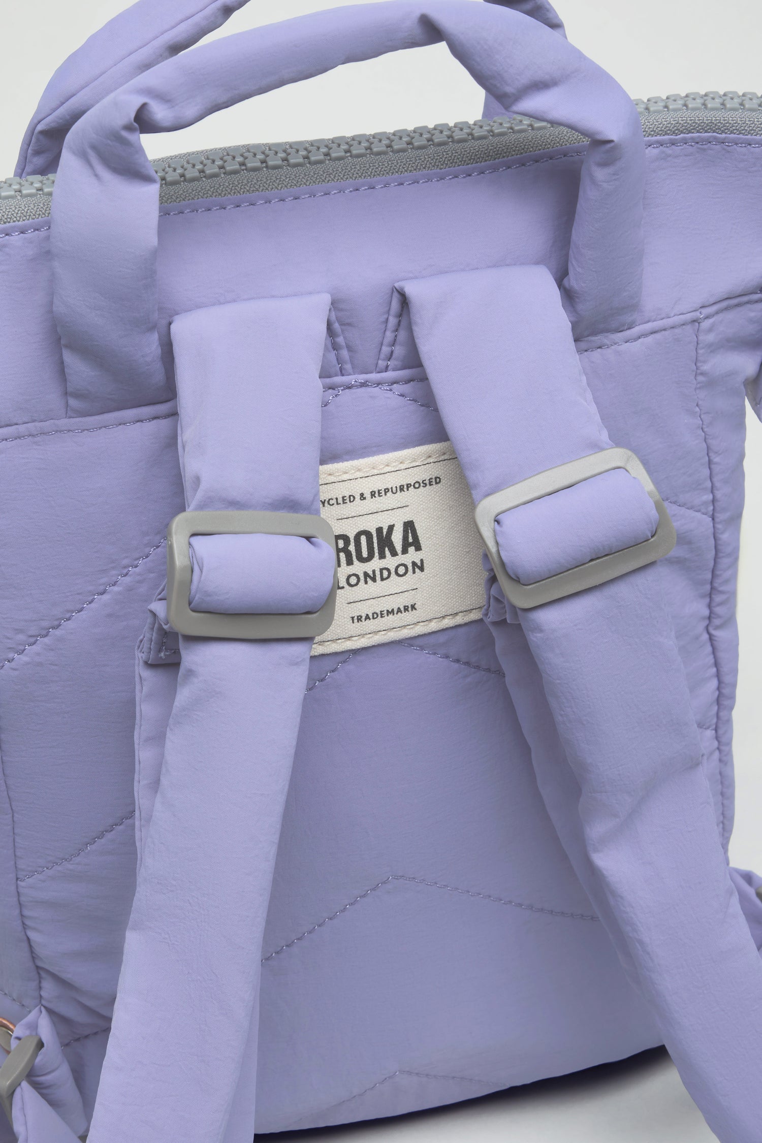 Close-up of the back of a light purple Cosmic Recycled Mini Taslon Bantry Bag, showing padded shoulder straps and a label reading "Roka London.