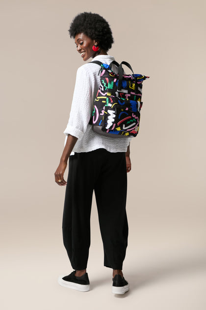 A woman wearing black pants and a Recycled Canfield Scribble Print Bag made from recycled bottles.