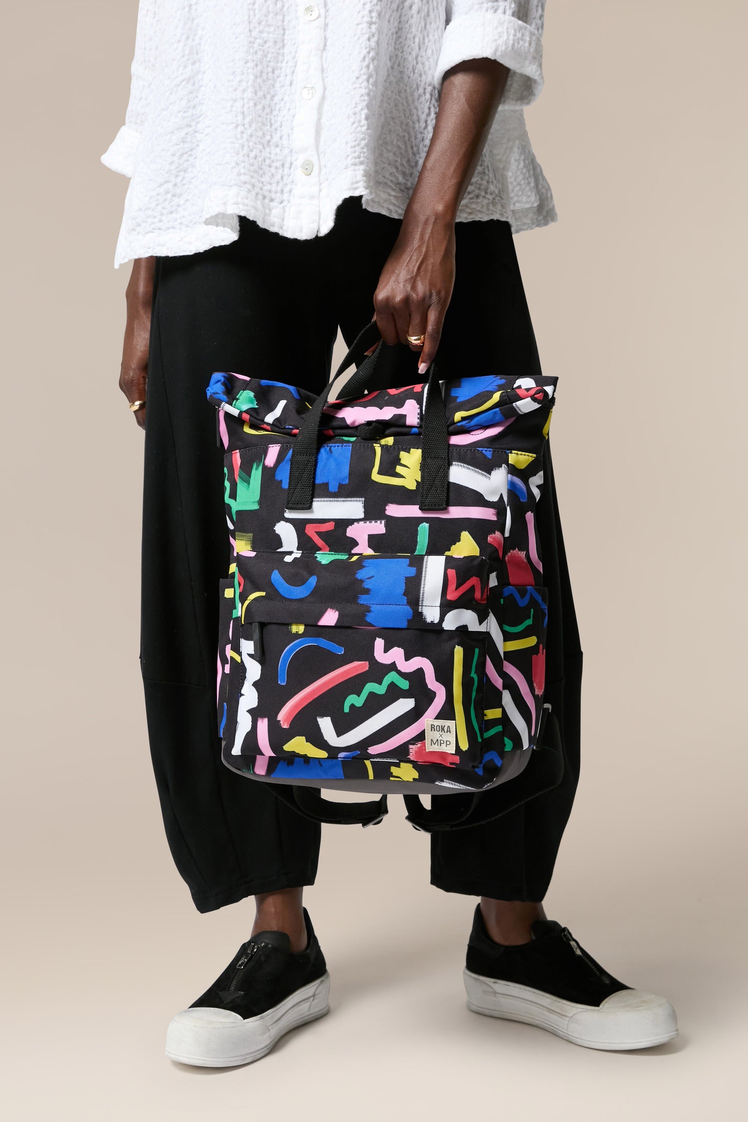 A woman is holding a colorful Recycled Canfield Scribble Print Bag made from recycled bottles.