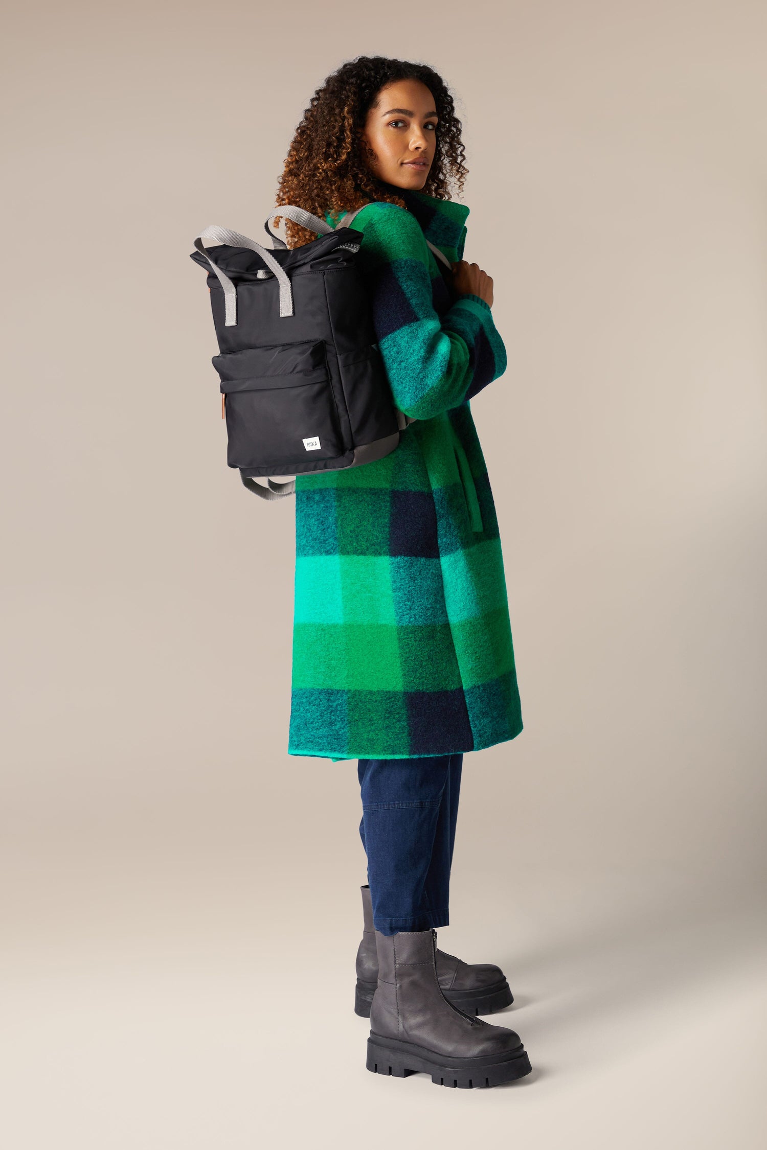 A woman wearing a green plaid coat and the Recycled Canfield Bag backpack.