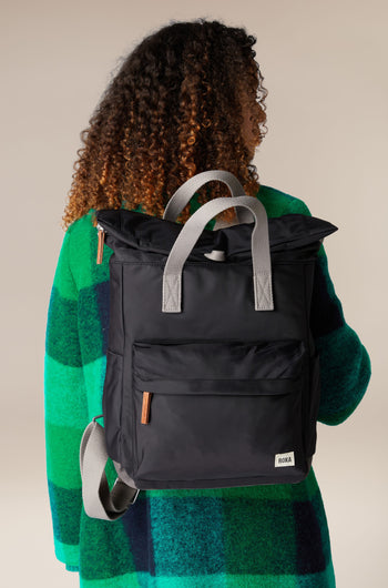 A woman wearing a green sweater carries a Recycled Canfield Bag for convenient storage.