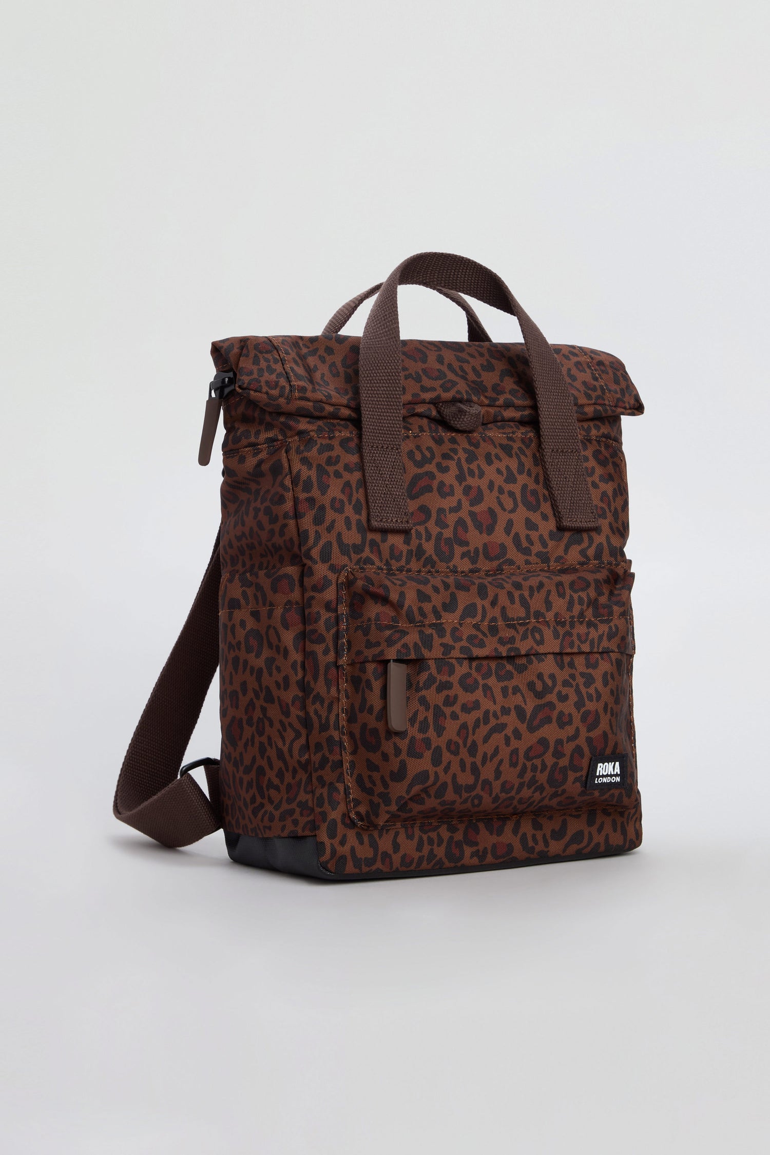The Mini Leopard Canfield Canvas Bag is a brown backpack with dark leopard spots, made from recycled canvas and featuring a front pocket, top handles, and a shoulder strap. It is displayed against a plain light background.