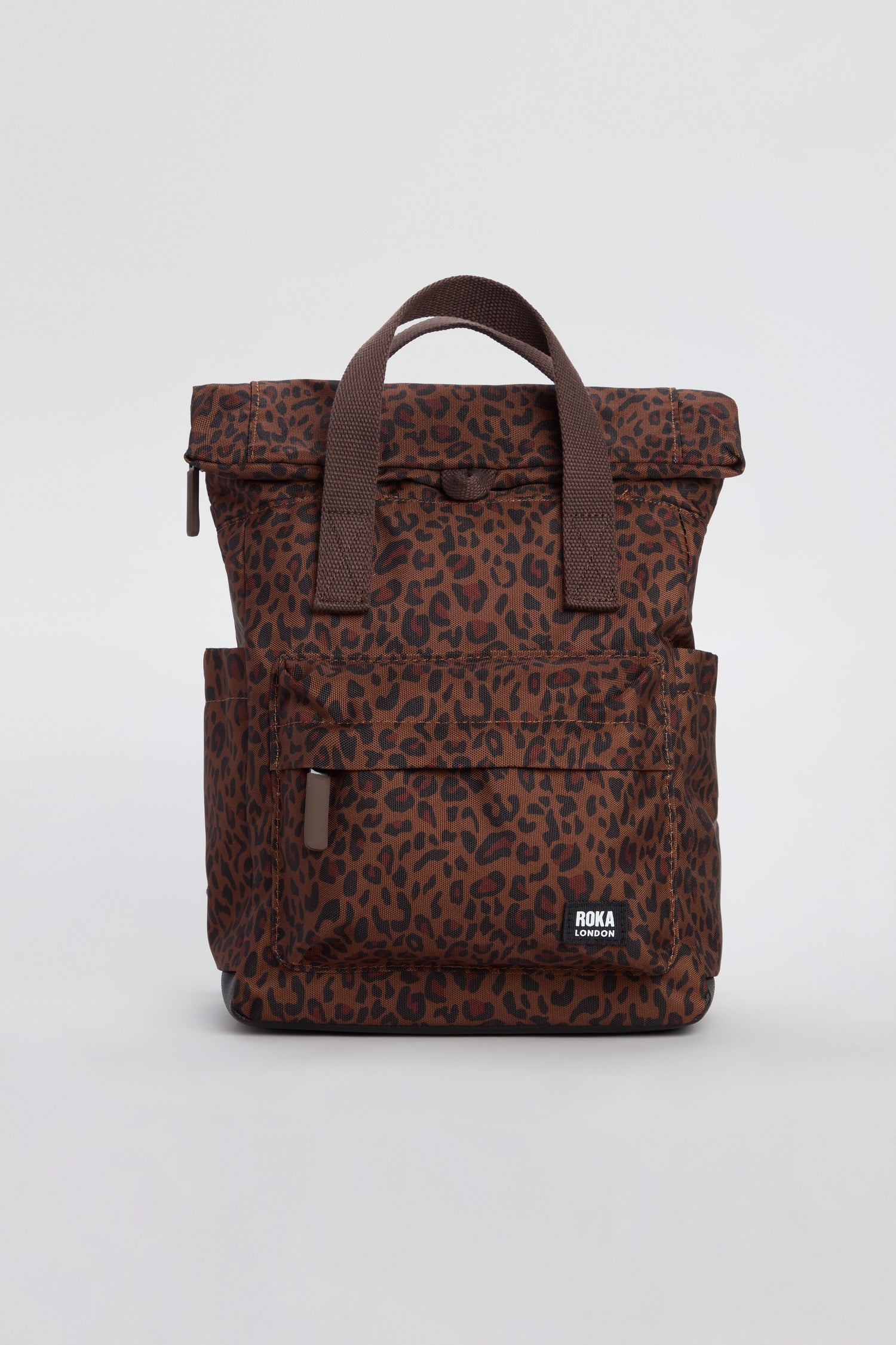 Introducing the Mini Leopard Canfield Canvas Bag—a stylish brown leopard print backpack made from recycled canvas, featuring two handles, a front zip pocket, handy side pockets, and a prominent “ROKA” logo patch.