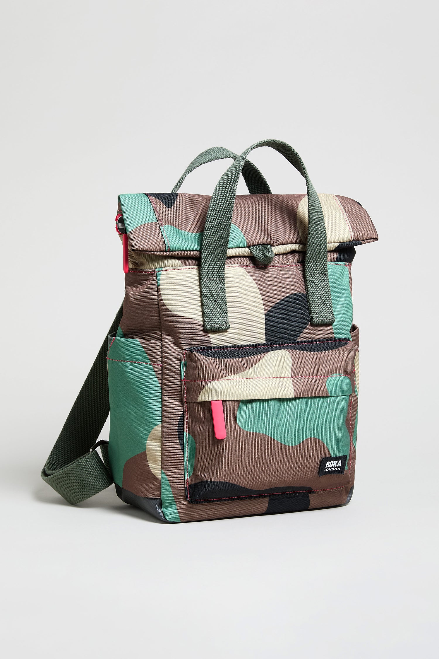 The Recycled Canvas Canfield Bag is a camouflage-patterned, water-repellent backpack with green handles, a front zipper pocket, side pockets, and a small black brand label on the front.