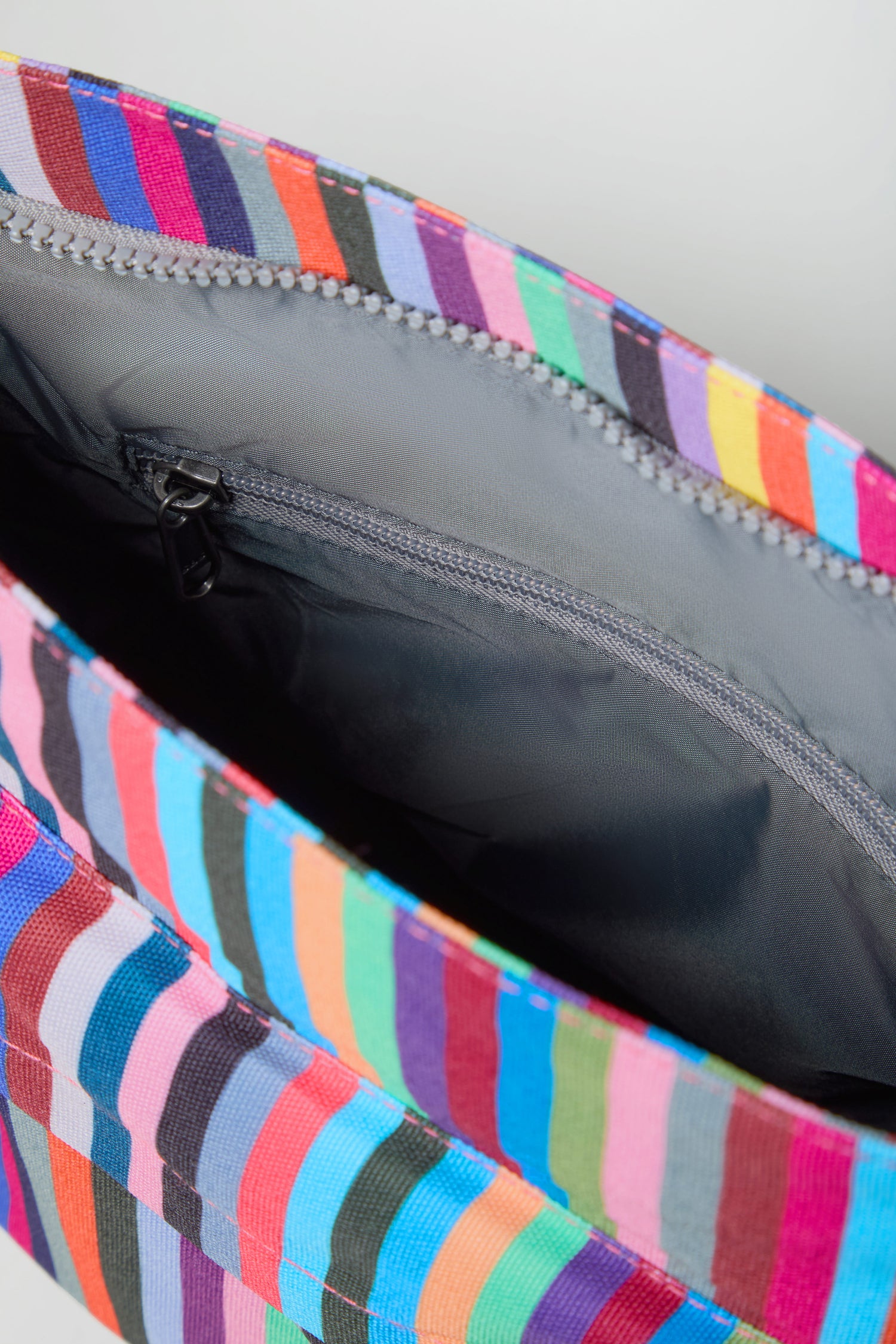 Close-up of the inside of the Recycled Canvas Kennington Bag, featuring a gray lining and a zippered pocket within its colorful, striped recycled canvas exterior.