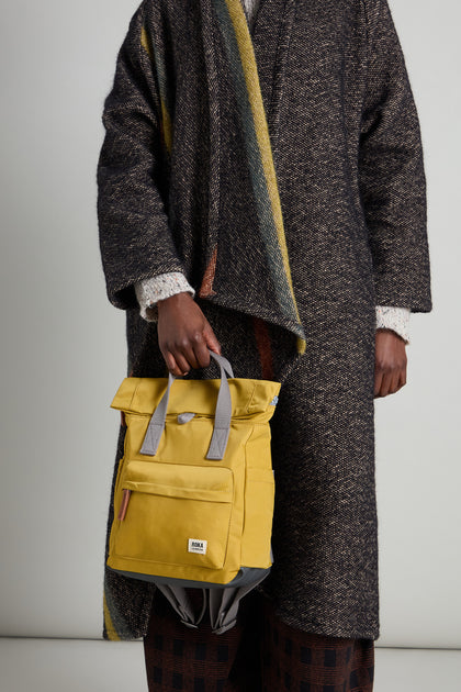 A person is holding the Recycled Nylon Small Canfield Bag in a vibrant yellow, highlighting its eco-friendly charm.