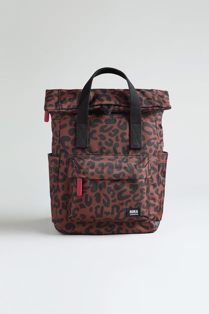 The Recycled Canvas Canfield Leopard Backpack features a brown leopard print, black handles, front and side pockets, and a water-resistant finish, displayed on a plain light background.