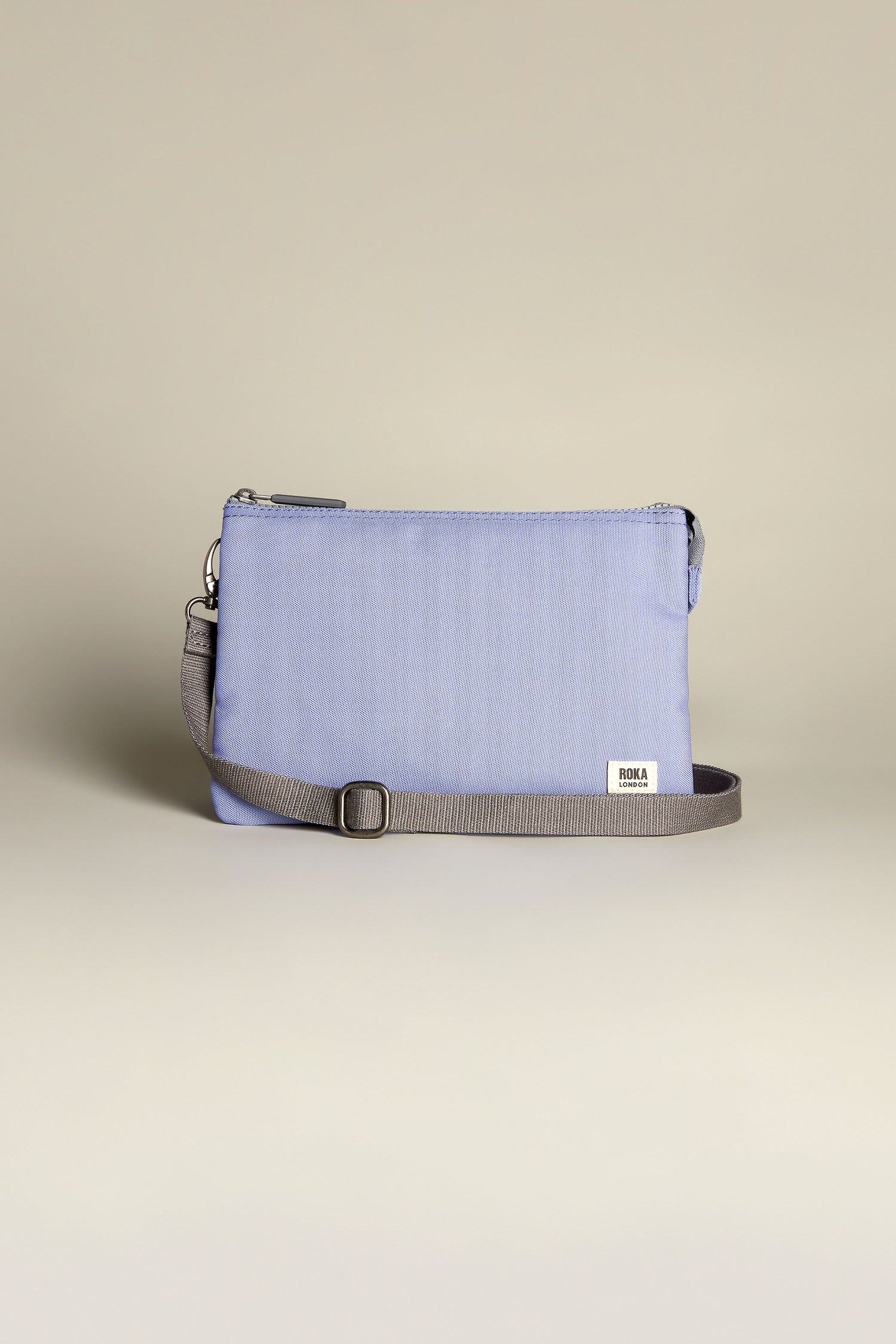 The Recycled Canvas Carnaby Crossbody Bag is a small rectangular shoulder bag in light blue, made with recycled canvas and featuring an adjustable gray crossbody strap, elegantly showcased against a neutral backdrop.