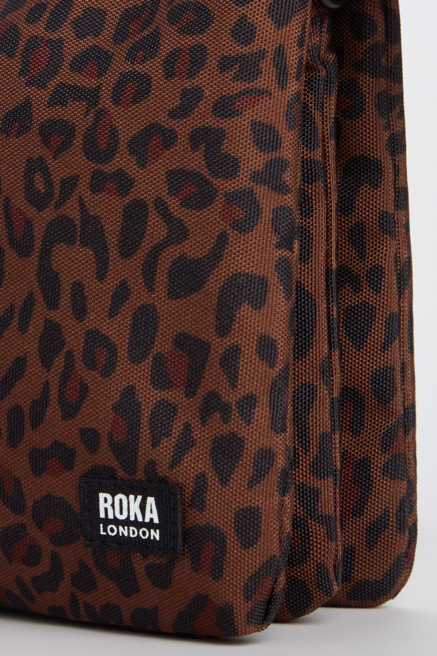 Close-up of the Mini Leopard Carnaby Crossbody Canvas Bag, featuring a brown leopard print, a “ROKA LONDON” label on the front corner, and crafted from recycled canvas for eco-friendly style.