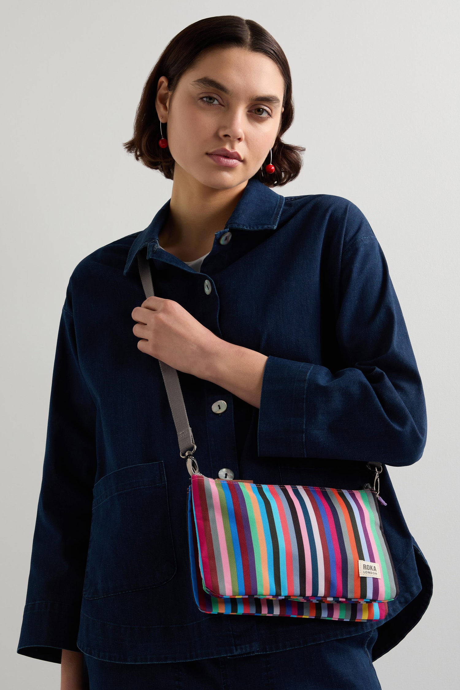 A person in a navy outfit carries the Multi Stripe Recycled Canvas Carnaby Crossbody Bag.