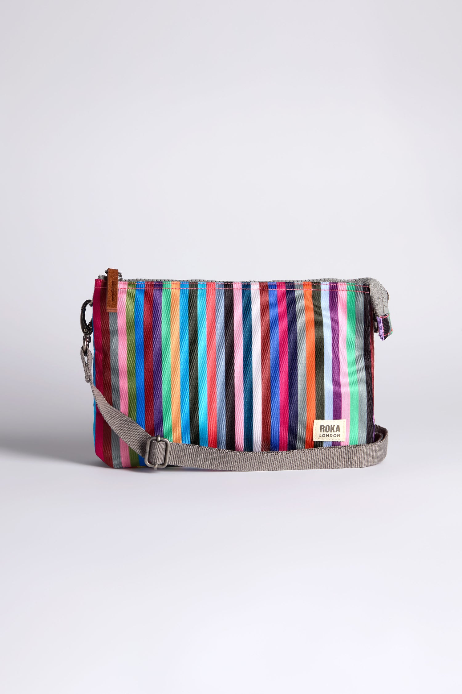 The Recycled Canvas Carnaby Crossbody Bag features a compact rectangular shape, multi-colored vertical stripes, gray zipper and adjustable strap. Made from weather-resistant recycled canvas, it's shown on a plain light background.