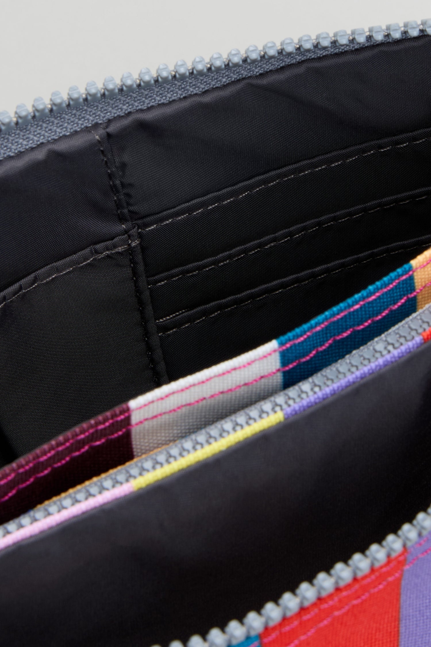 Close-up of an open Wide Multistripe Carnaby Crossbody Canvas Bag featuring a multicolored, weather-resistant recycled canvas exterior and visible inner card slots stitched onto the black lining.