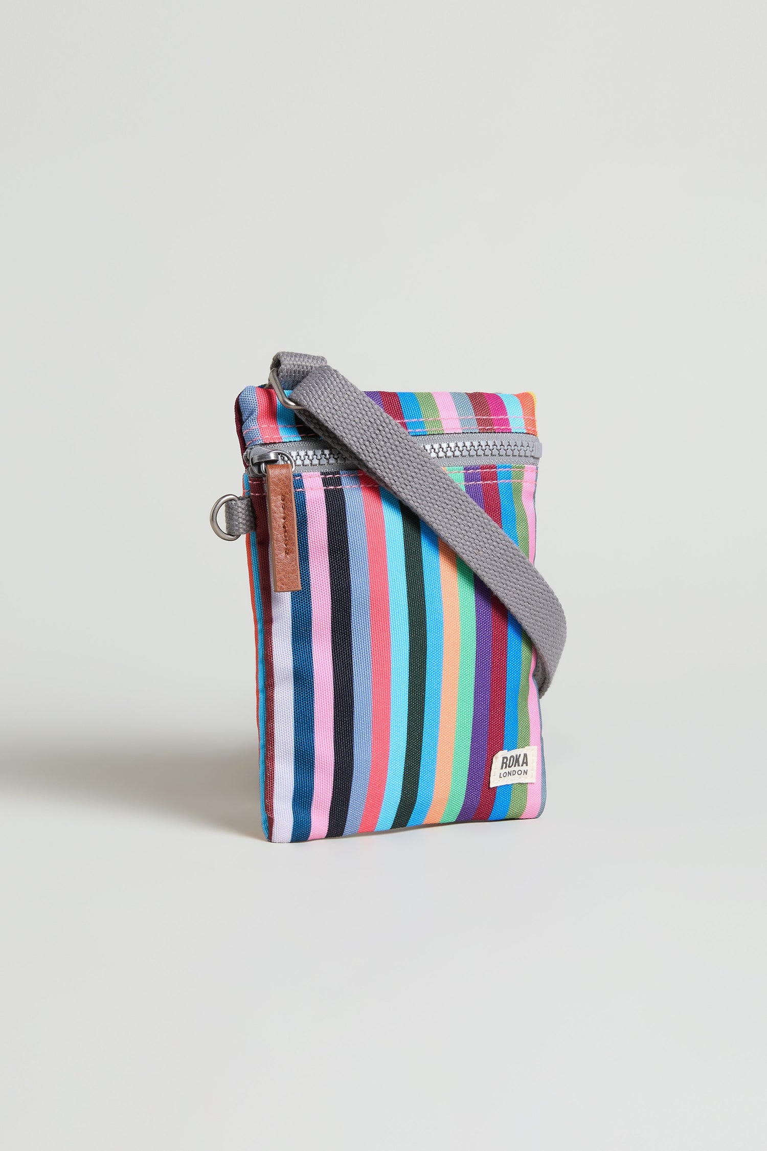The Recycled Canvas Chelsea Bag is a compact, weather-resistant crossbody with multicolored vertical stripes, a gray strap, and a visible ROKA label—perfect for carrying essentials hands-free.