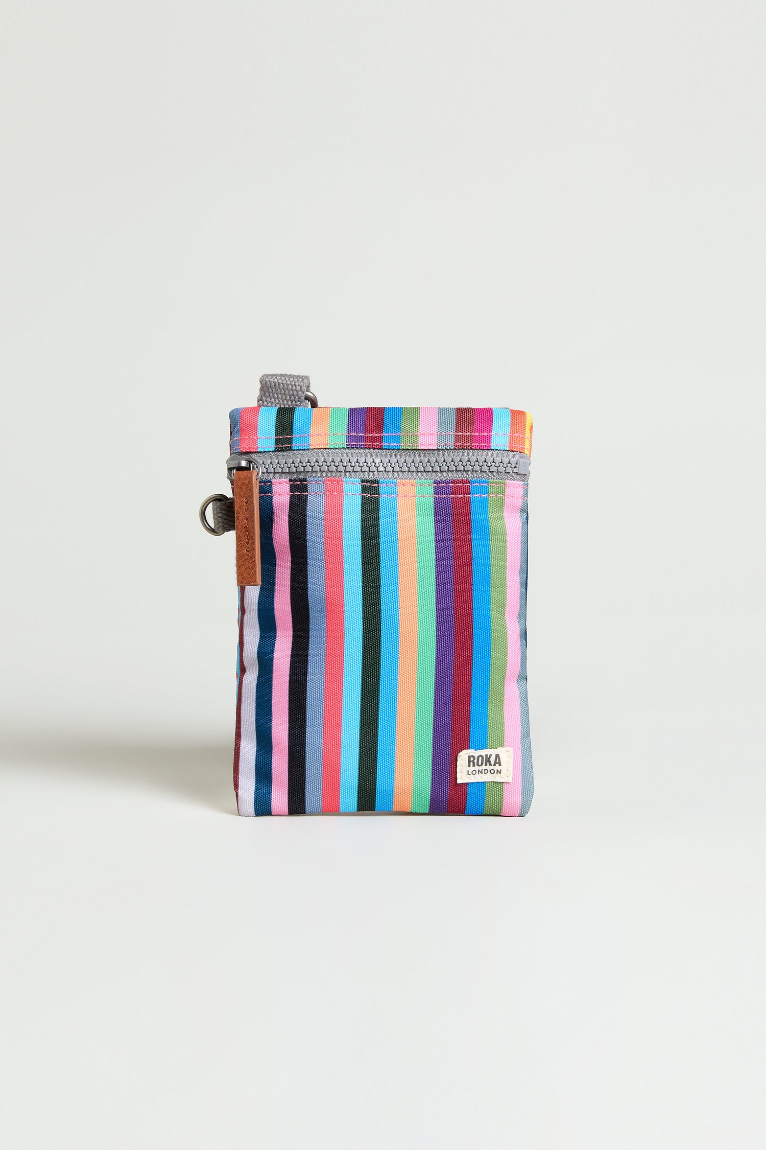 The Recycled Canvas Chelsea Bag is a small zippered pouch with vertical multicolored stripes, gray zipper, brown pull tab, metal ring attachment, and a "ROKA" label on the front—ideal for carrying essentials on the go.
