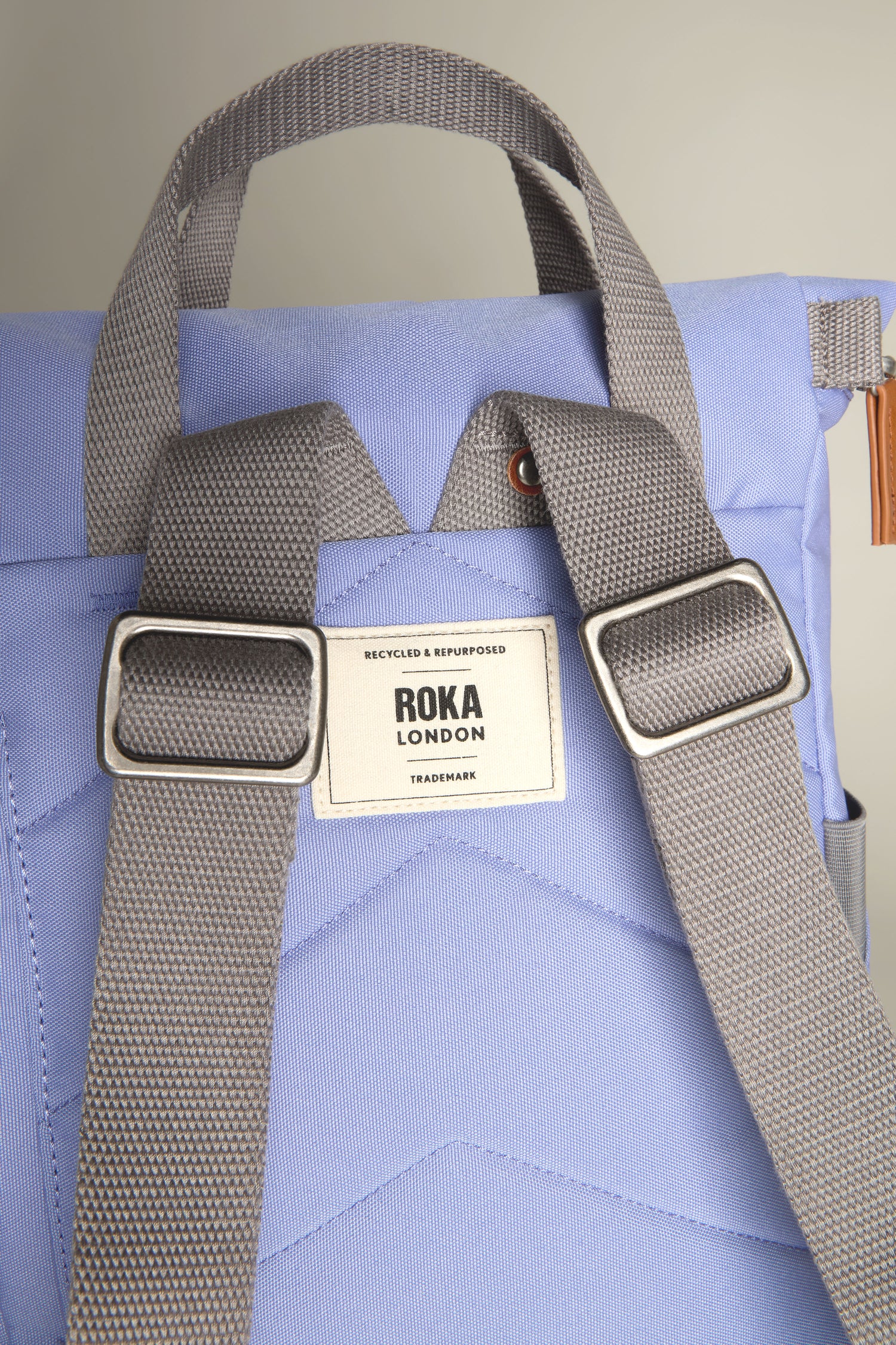 Close-up of a light blue Recycled Canvas Small Finchley Bag with gray straps and a "ROKA LONDON" label on the back. This sustainable bag is designed for the eco-conscious modern traveler.