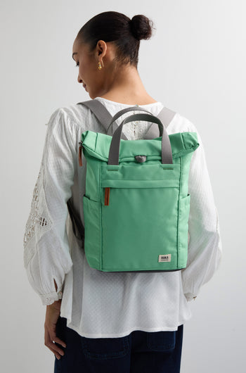 Wearing a Recycled Canvas Small Finchley Bag in green with gray straps over a white textured blouse, a person embraces sustainable fashion with every step.