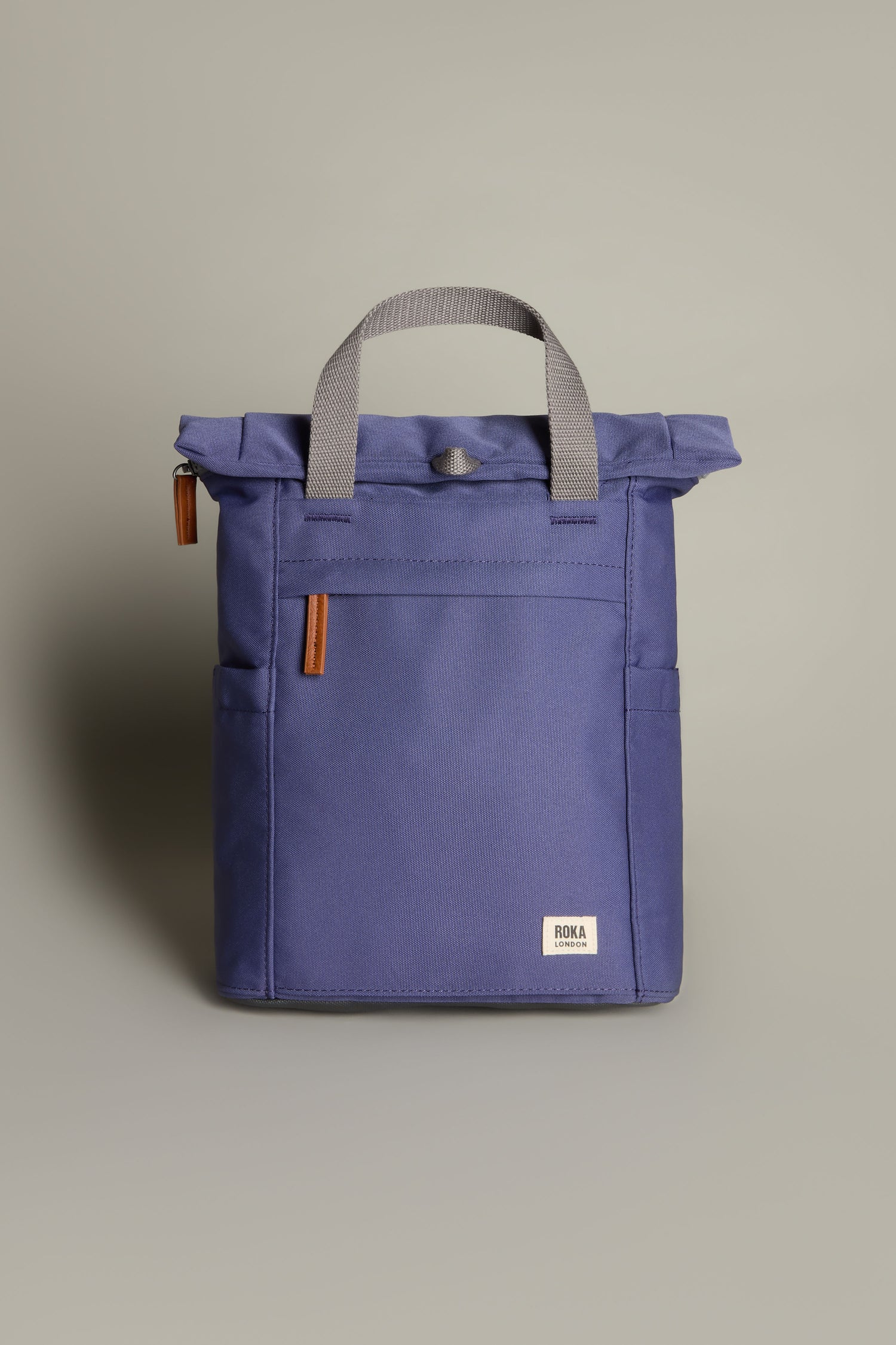 The Recycled Canvas Small Finchley Bag is a blue, square-shaped backpack made from recycled canvas featuring gray handles and brown zipper pulls, reflecting its commitment to sustainability.