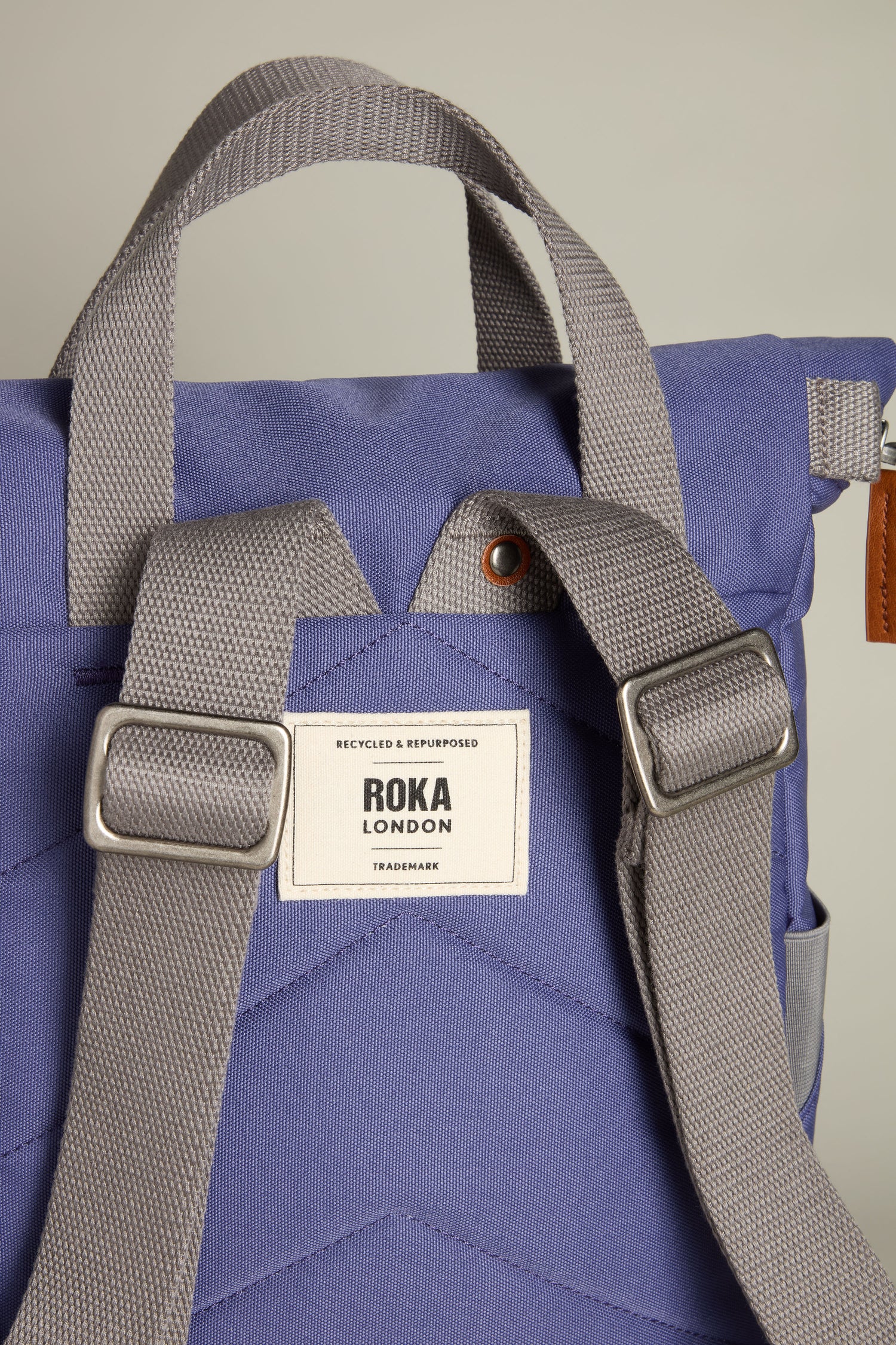 Close-up of a blue-gray Recycled Canvas Small Finchley Bag with adjustable straps and a "Roka London" label, highlighting its sustainable, eco-friendly design.