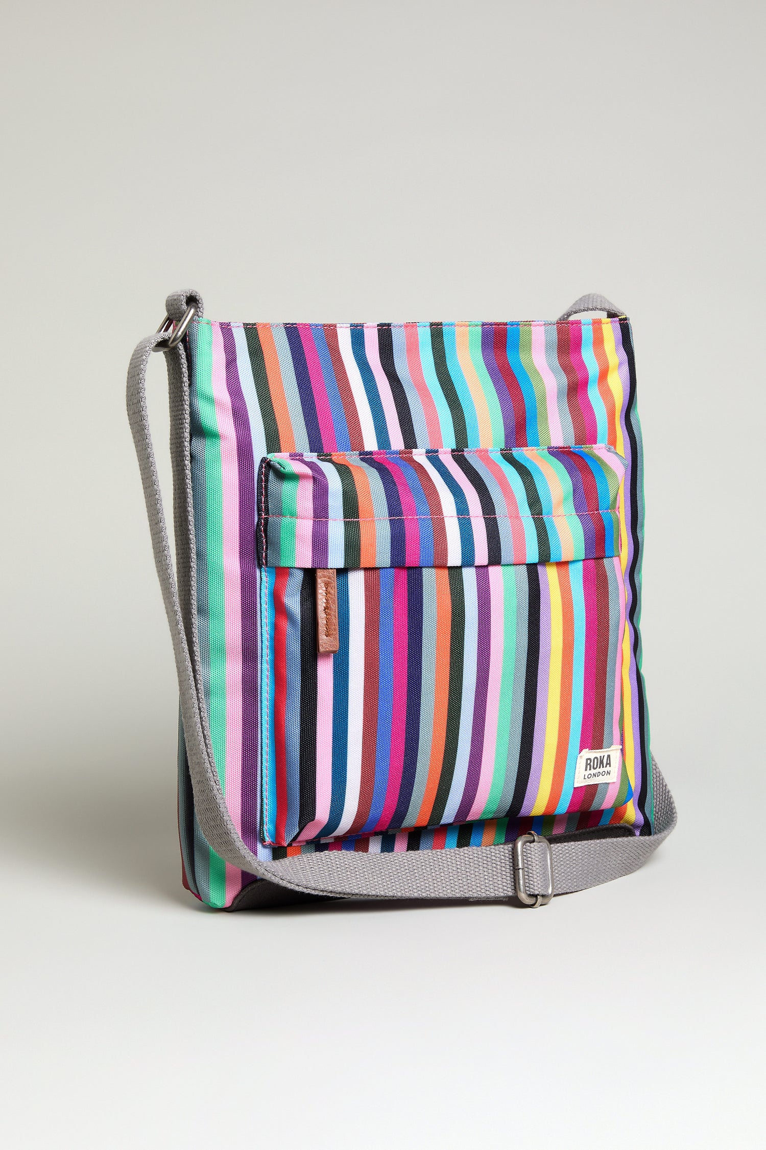The Recycled Canvas Kennington Bag is a sustainable crossbody featuring vertical multicolored stripes, a gray strap, and a front pocket, displayed against a plain light background.