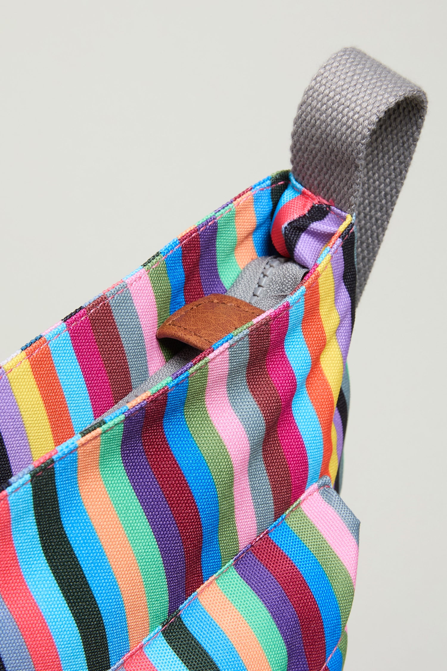 Close-up of the Recycled Canvas Kennington Bag, featuring multicolored vertical stripes, a gray woven handle, and a brown leather accent near the opening.