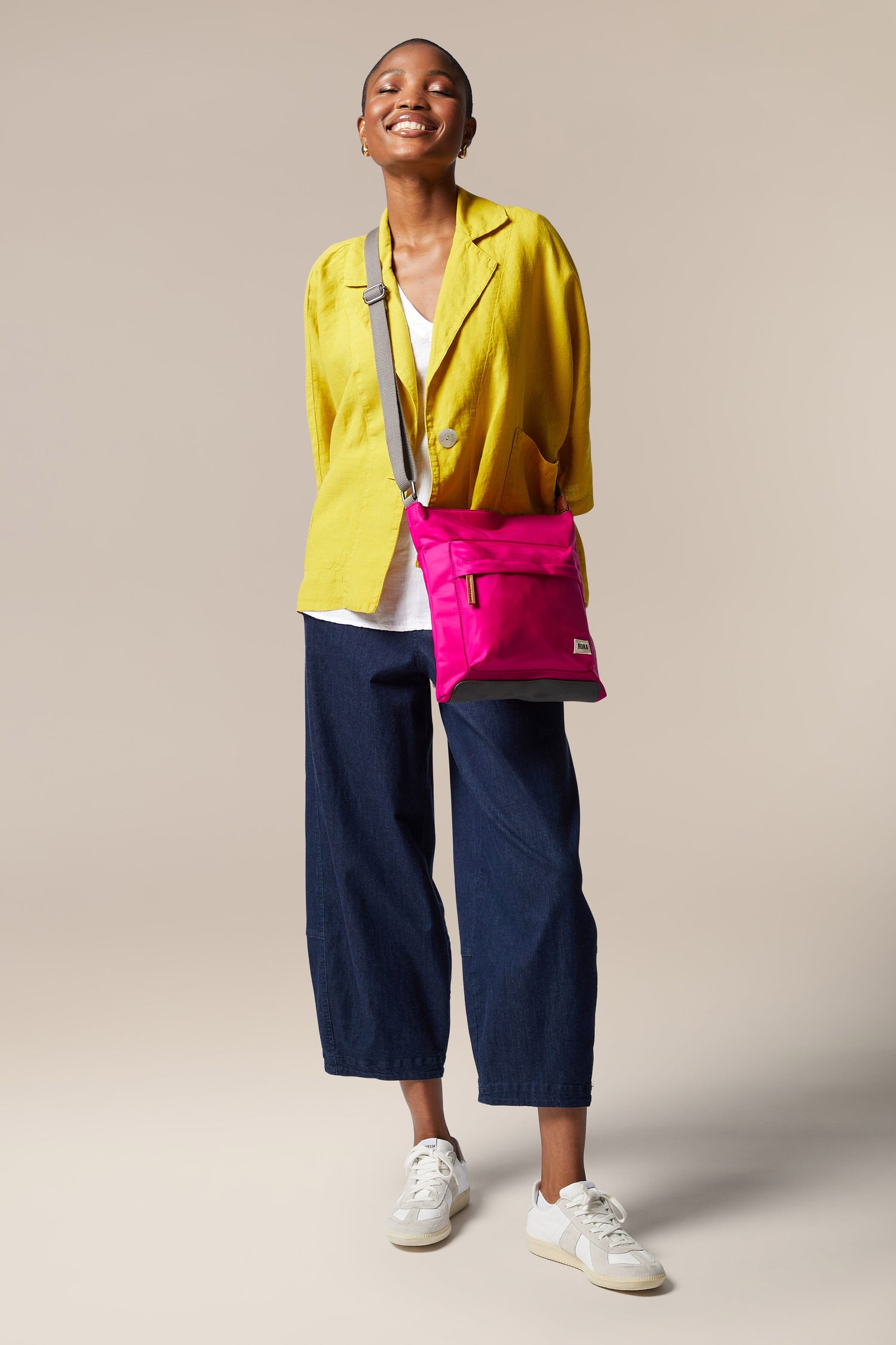 A woman in a yellow jacket and jeans carrying a Kennington Crossbody Bag with an adjustable strap.