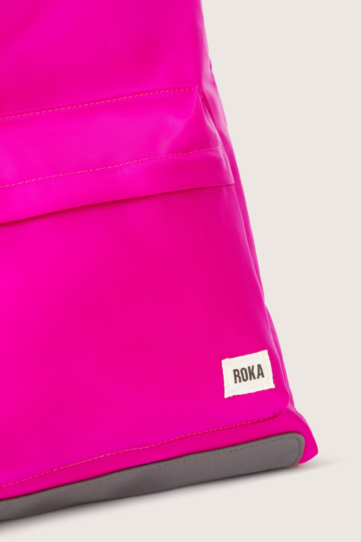 A sleek pink Kennington Crossbody Bag with an adjustable strap and the word roo on it.