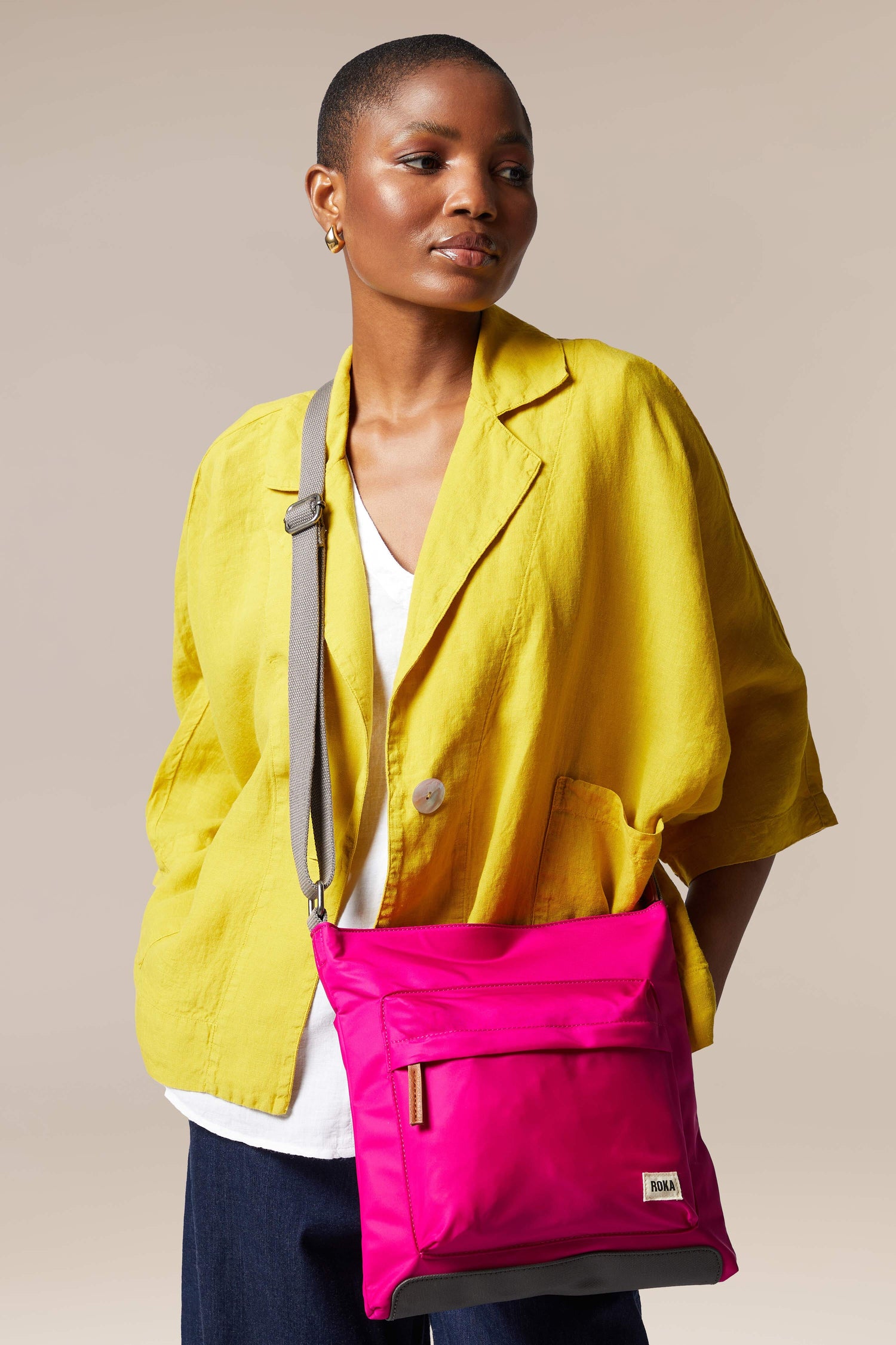 A woman wearing a sleek yellow jacket and carrying a Kennington Crossbody Bag with an adjustable strap.