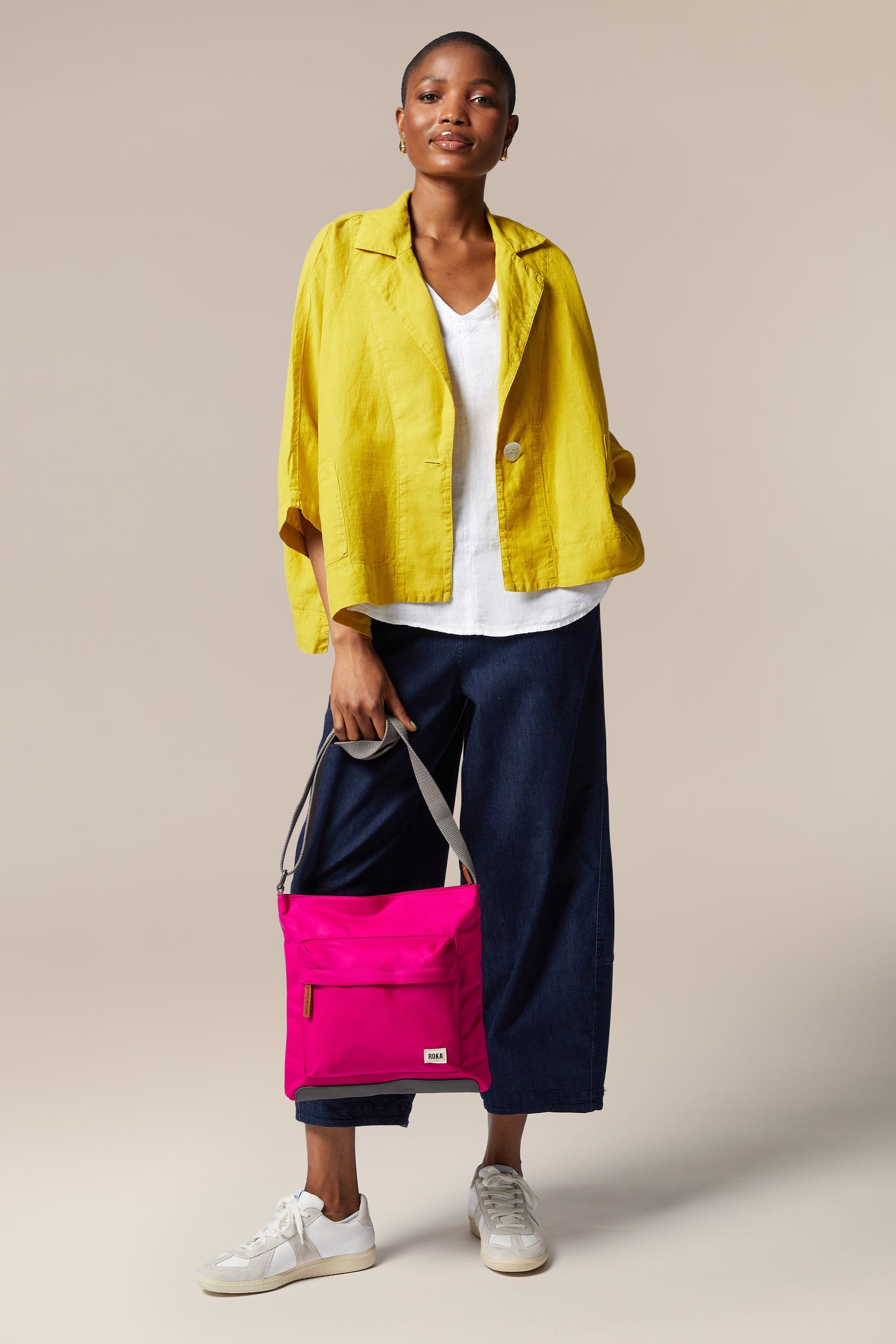 A woman is holding a sleek, bright pink Kennington Crossbody Bag with an adjustable strap.