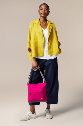 A woman in a pink jacket and yellow pants is holding a sleek Kennington Crossbody Bag.