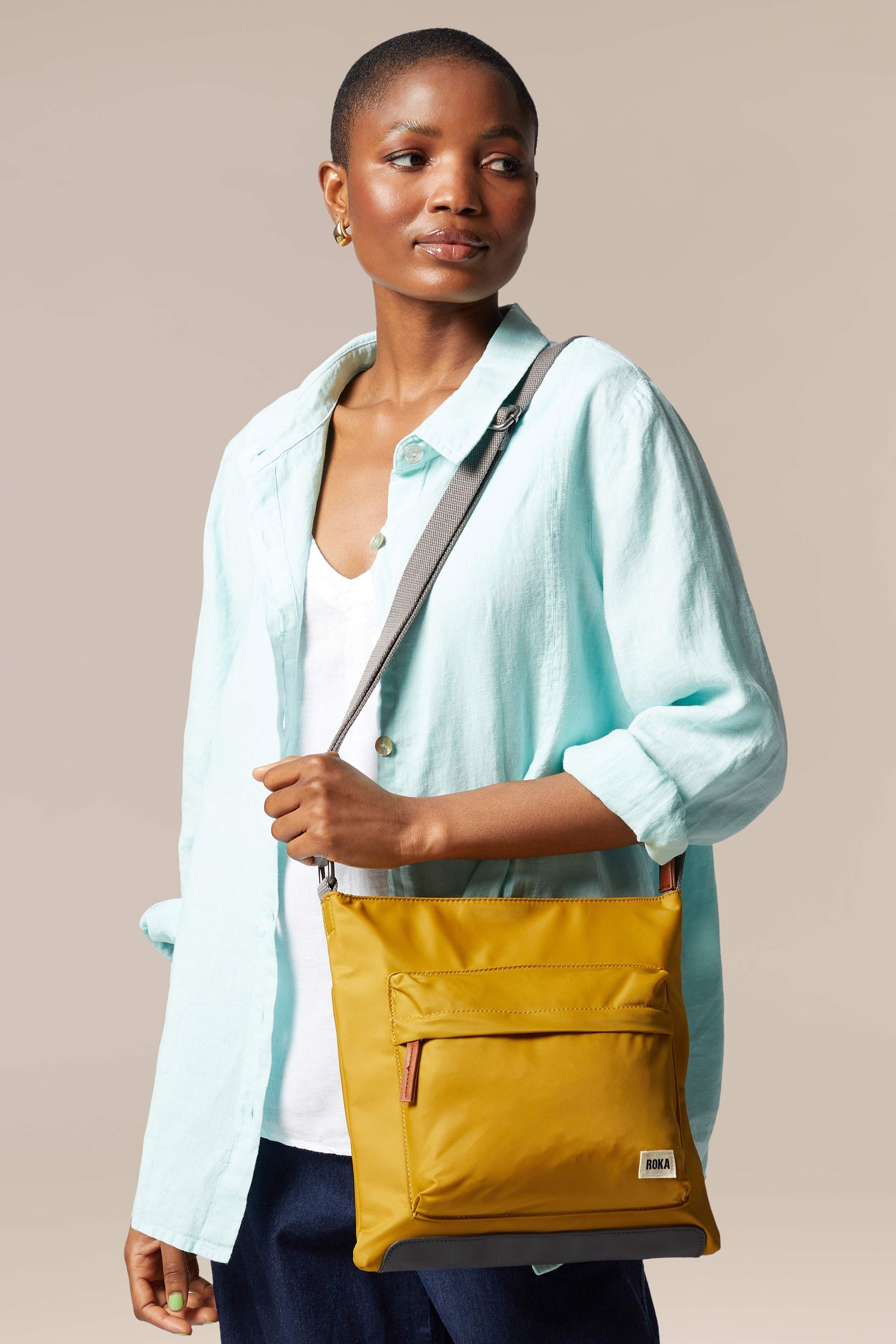 A woman is holding a sleek, yellow Kennington Crossbody Bag with an adjustable strap.