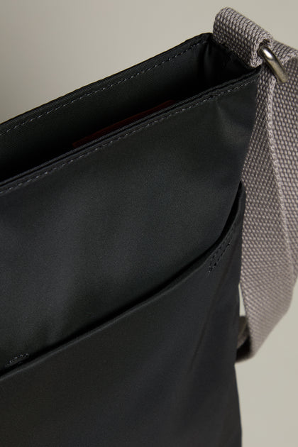 Close-up of the Recycled Nylon Kennington Crossbody Bag in sleek black, featuring a gray strap and an exterior pocket.