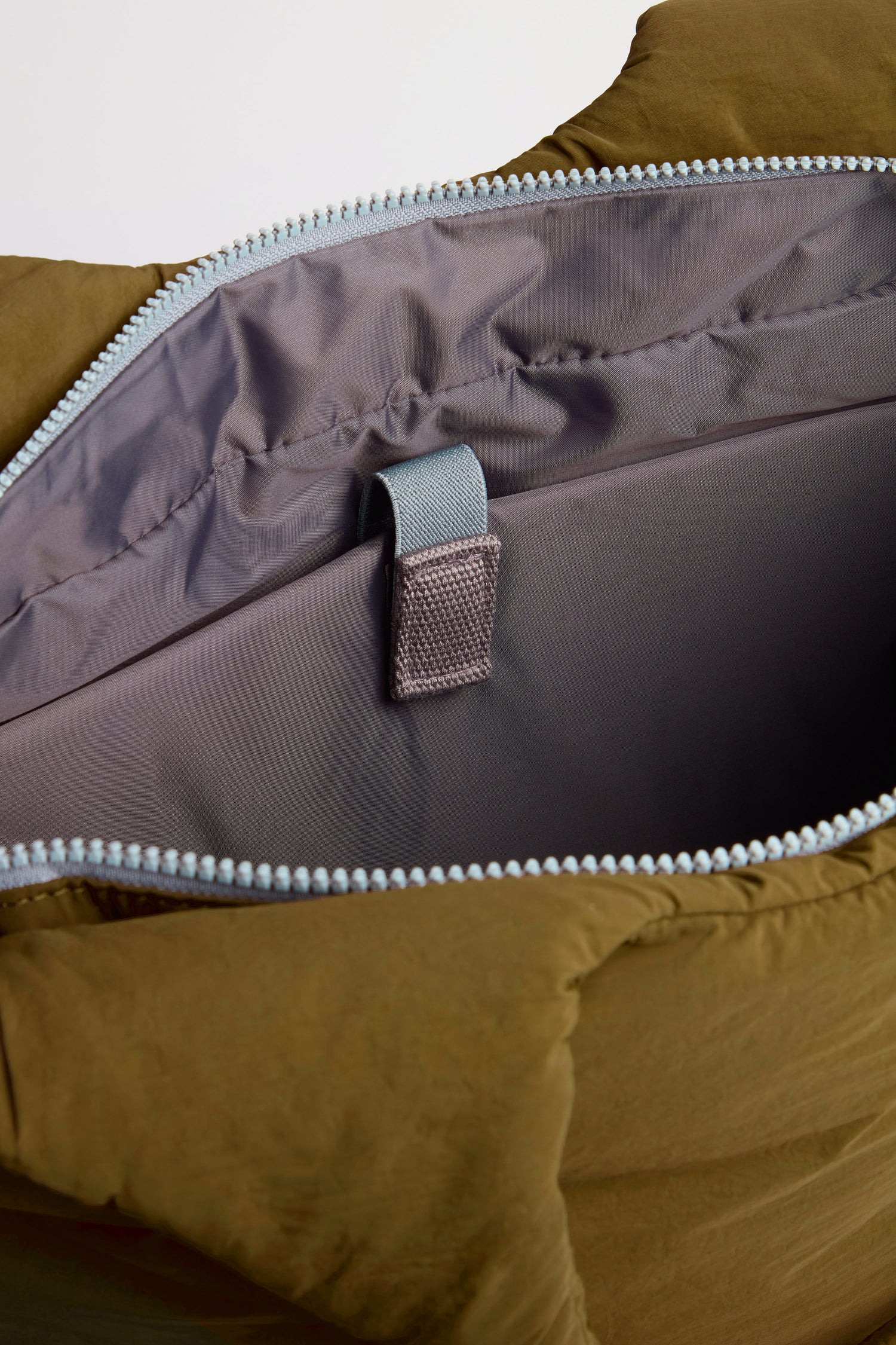 Close-up of an open Oxford Moss Shoulder Bag in olive green, highlighting the grey interior lining, a fabric loop, and a spacious inner compartment with a padded laptop sleeve.