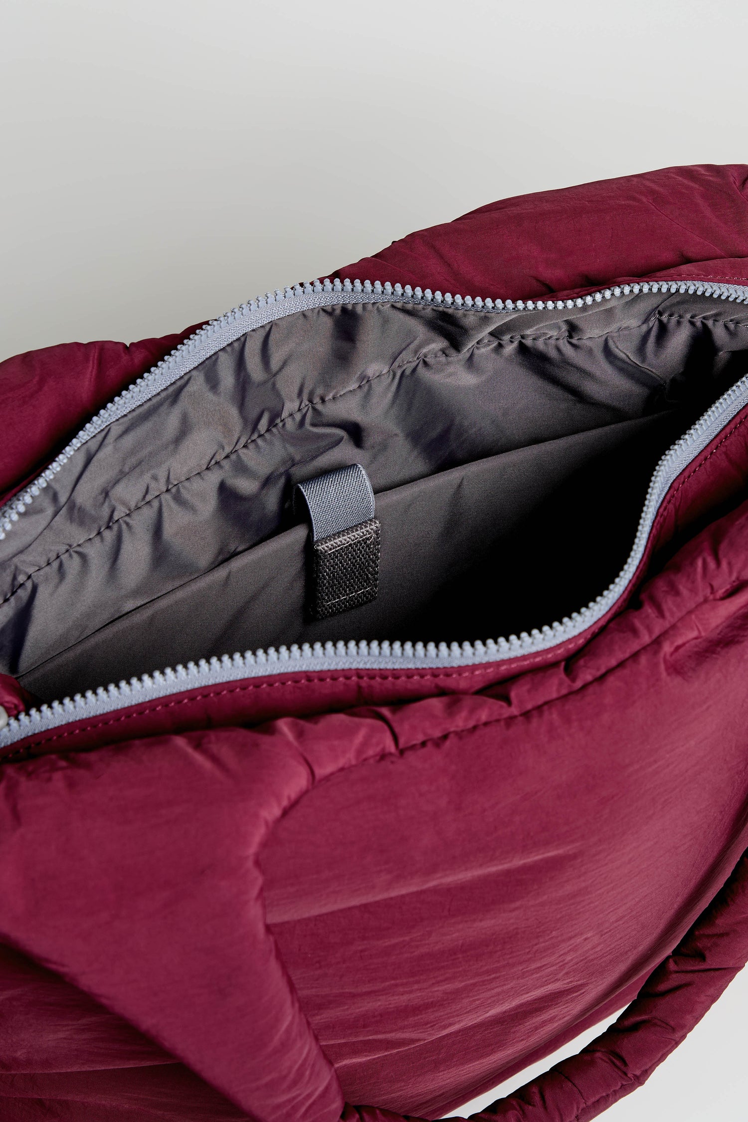 Close-up of an open Oxford Merlot Shoulder Bag, showcasing its gray interior with a zipper and an inner pocket, complemented by a black strap. This weather-resistant bag also features a padded laptop sleeve for added protection.