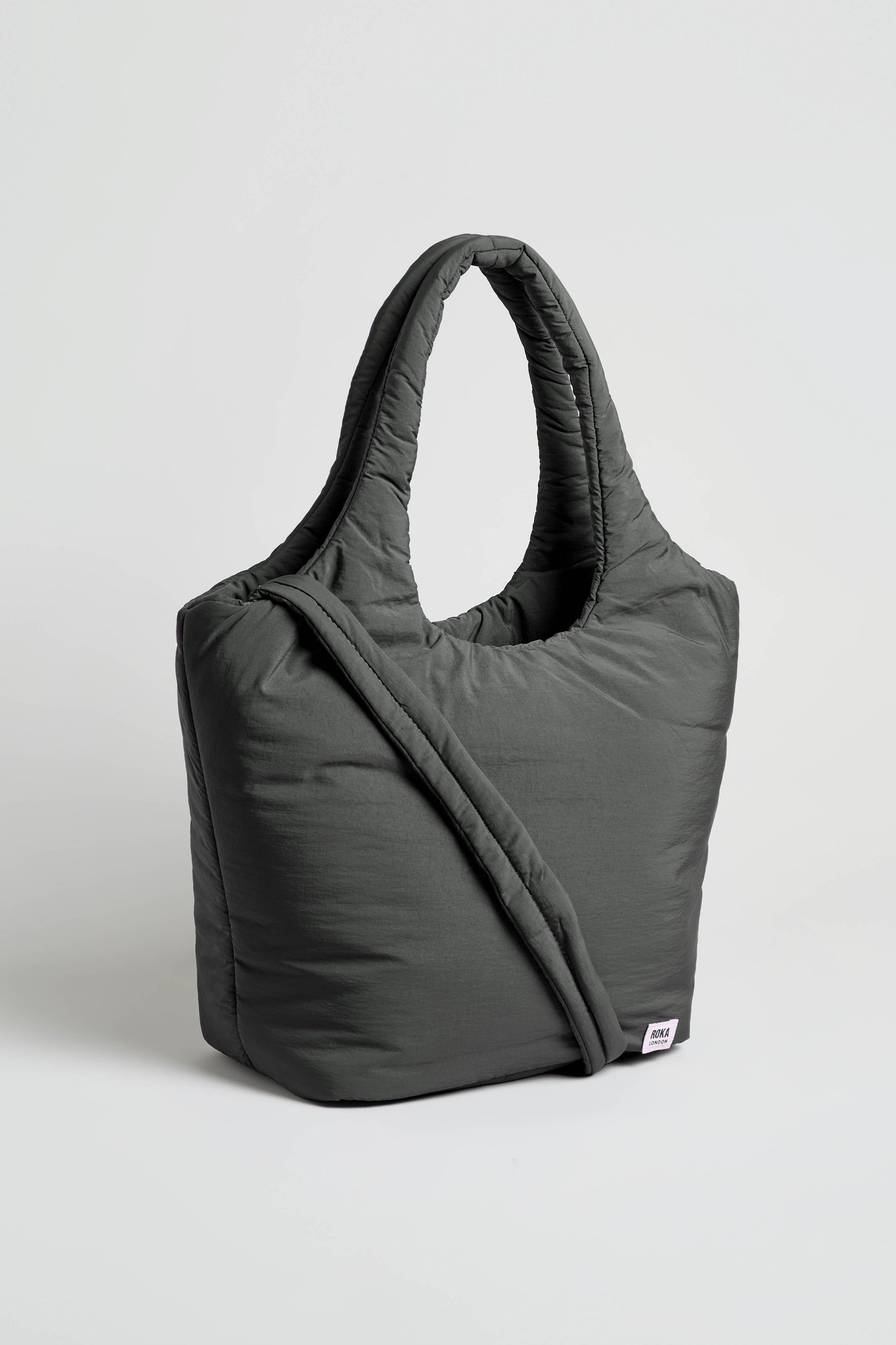 The Oxford Raven Shoulder Bag, in dark gray with quilted detailing, features two handles and a crossbody strap, plus a padded laptop sleeve for extra protection. It is shown standing upright against a plain white background.