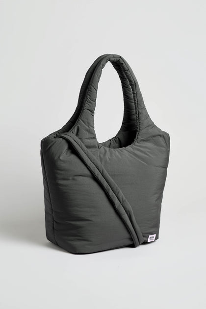 The Oxford Raven Shoulder Bag, in dark gray with quilted detailing, features two handles and a crossbody strap, plus a padded laptop sleeve for extra protection. It is shown standing upright against a plain white background.