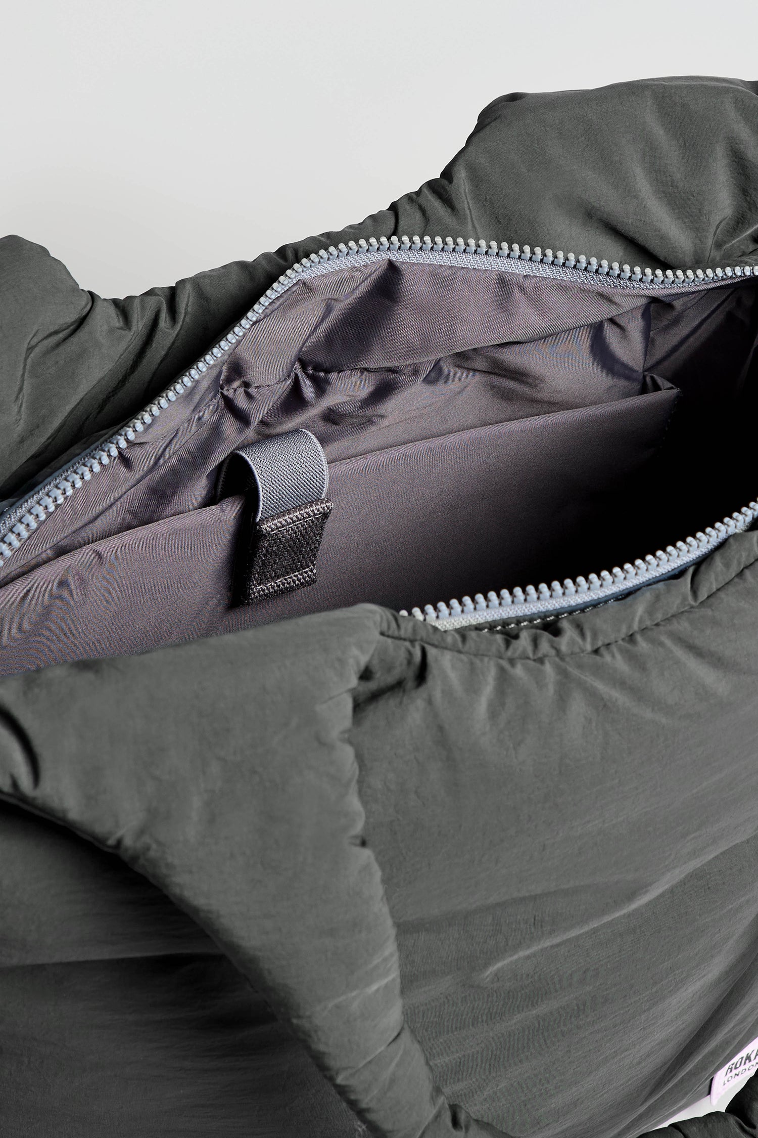 Close-up of an open, black Oxford Raven Shoulder Bag with a zippered design, revealing its empty interior, an internal fabric loop, and a padded laptop sleeve for extra protection.
