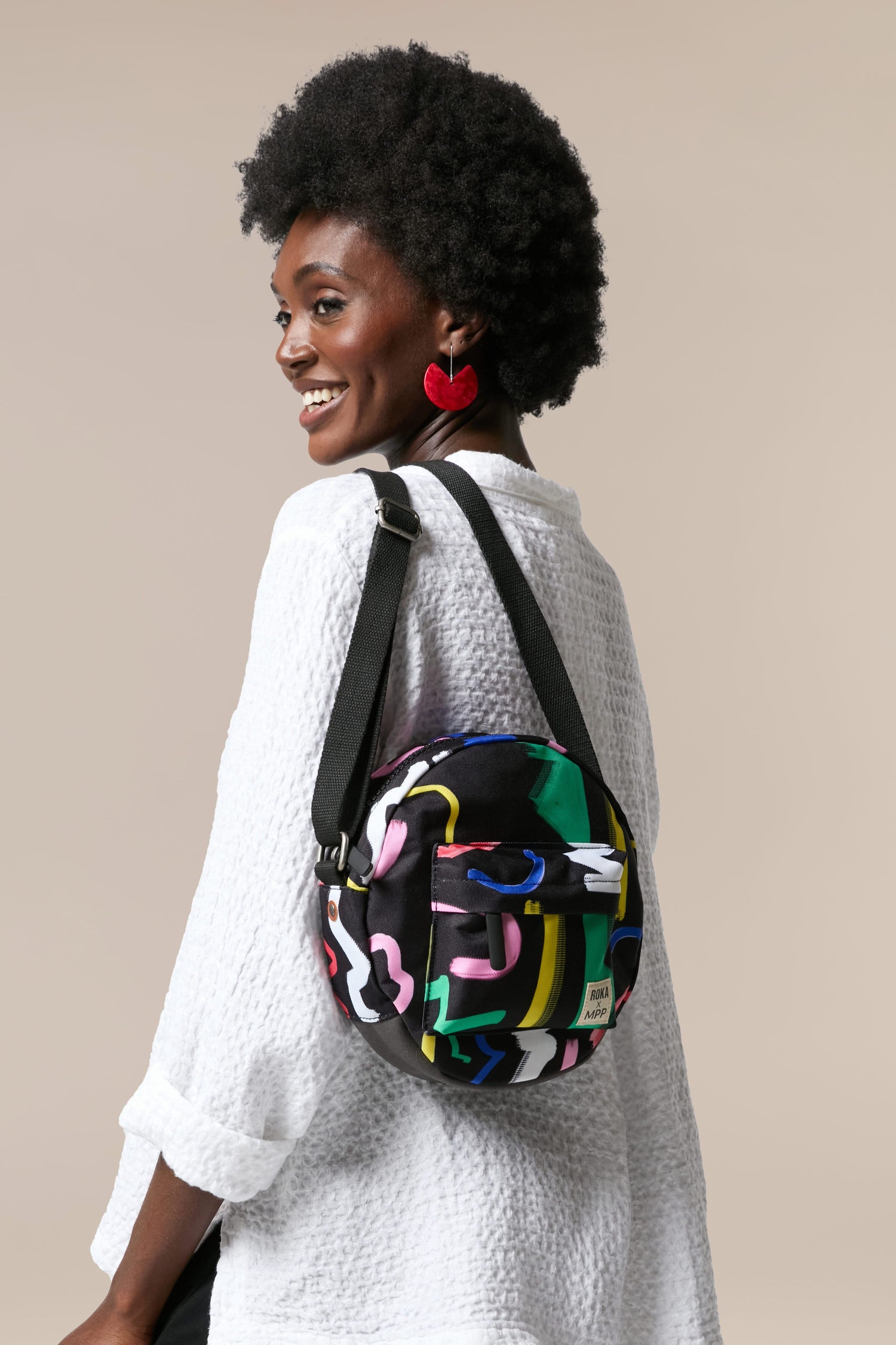 A weather-resistant woman wearing a colorful Recycled Scribble Print Paddington Bag with an afro hairstyle.